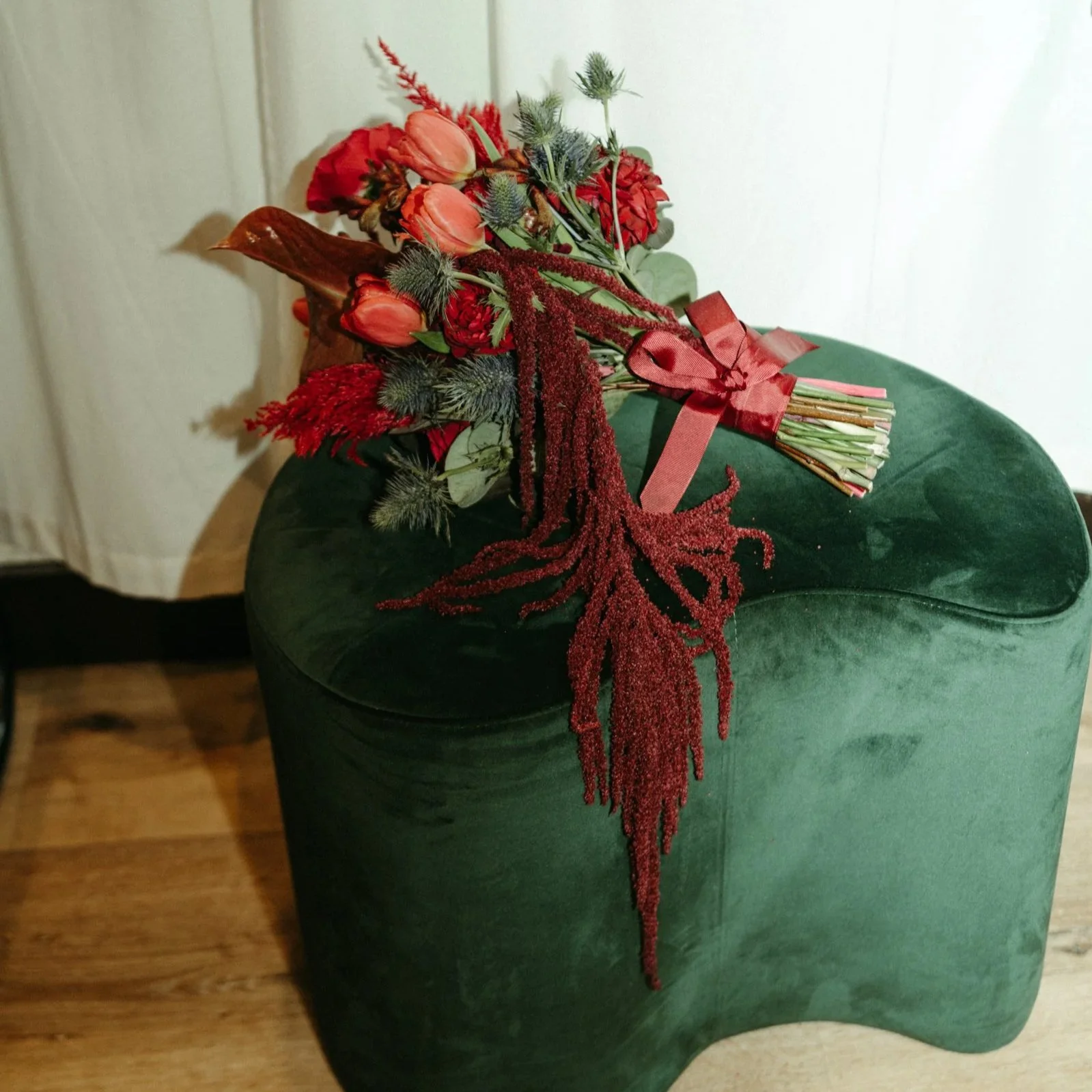 A bouquet of red flowers with green foliage resting on a dark green velvet ottoman.