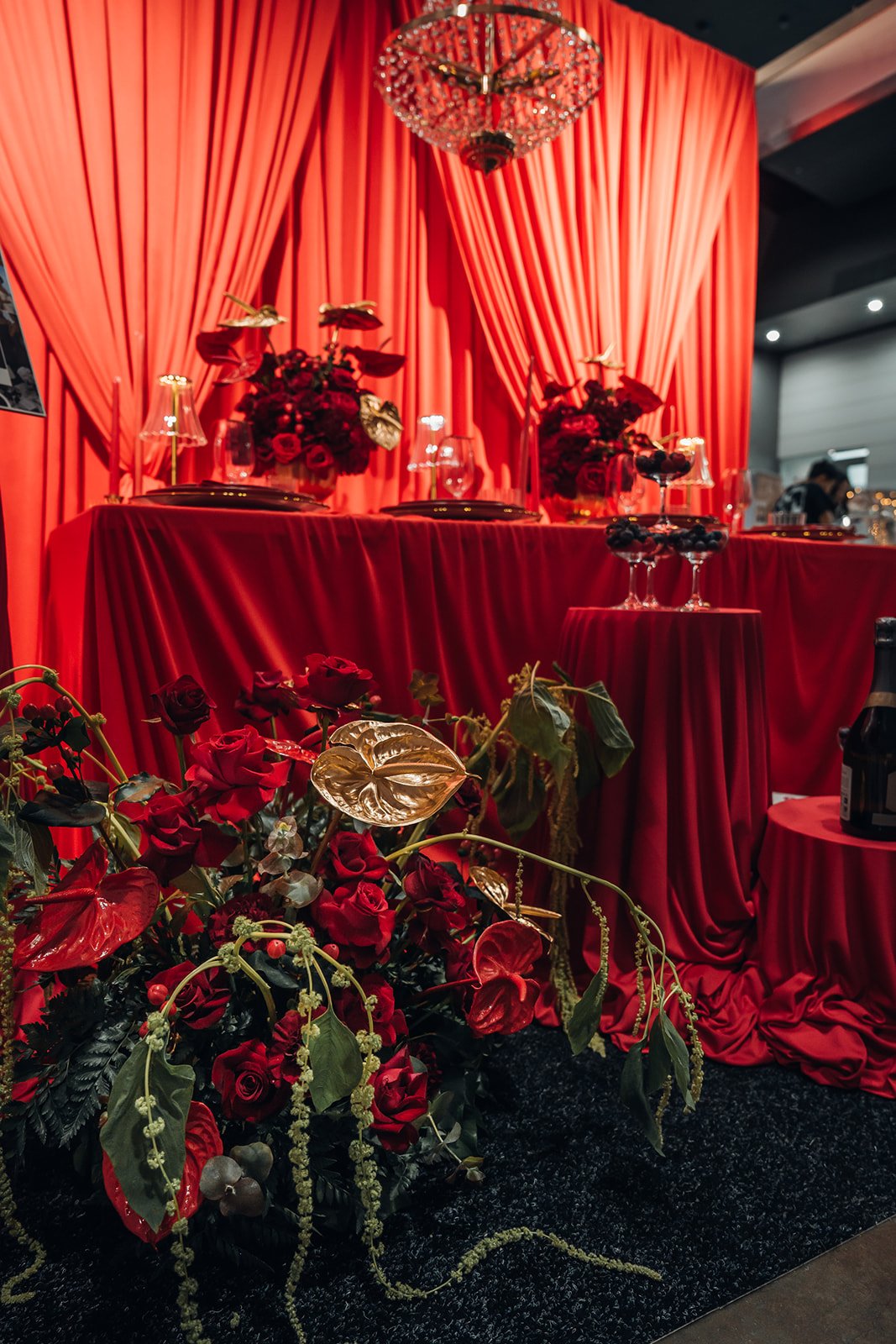 A luxurious event setup with red draped fabric, floral arrangements, and elegant table settings.