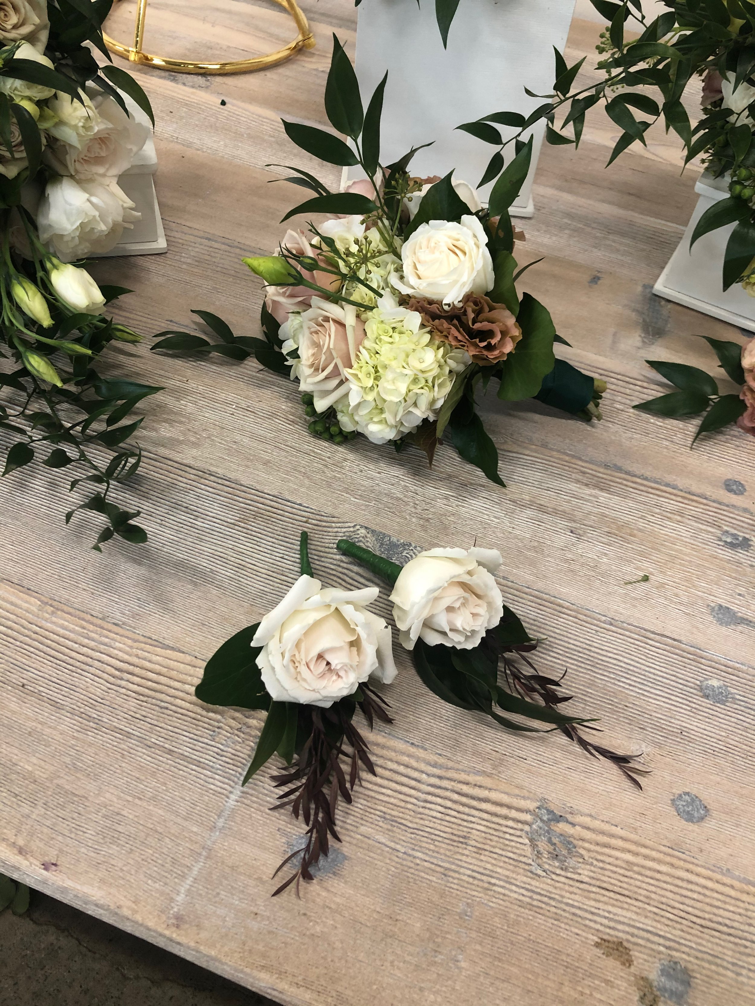 Cream-colored and light pink floral boutonniere with greenery on a wooden surface