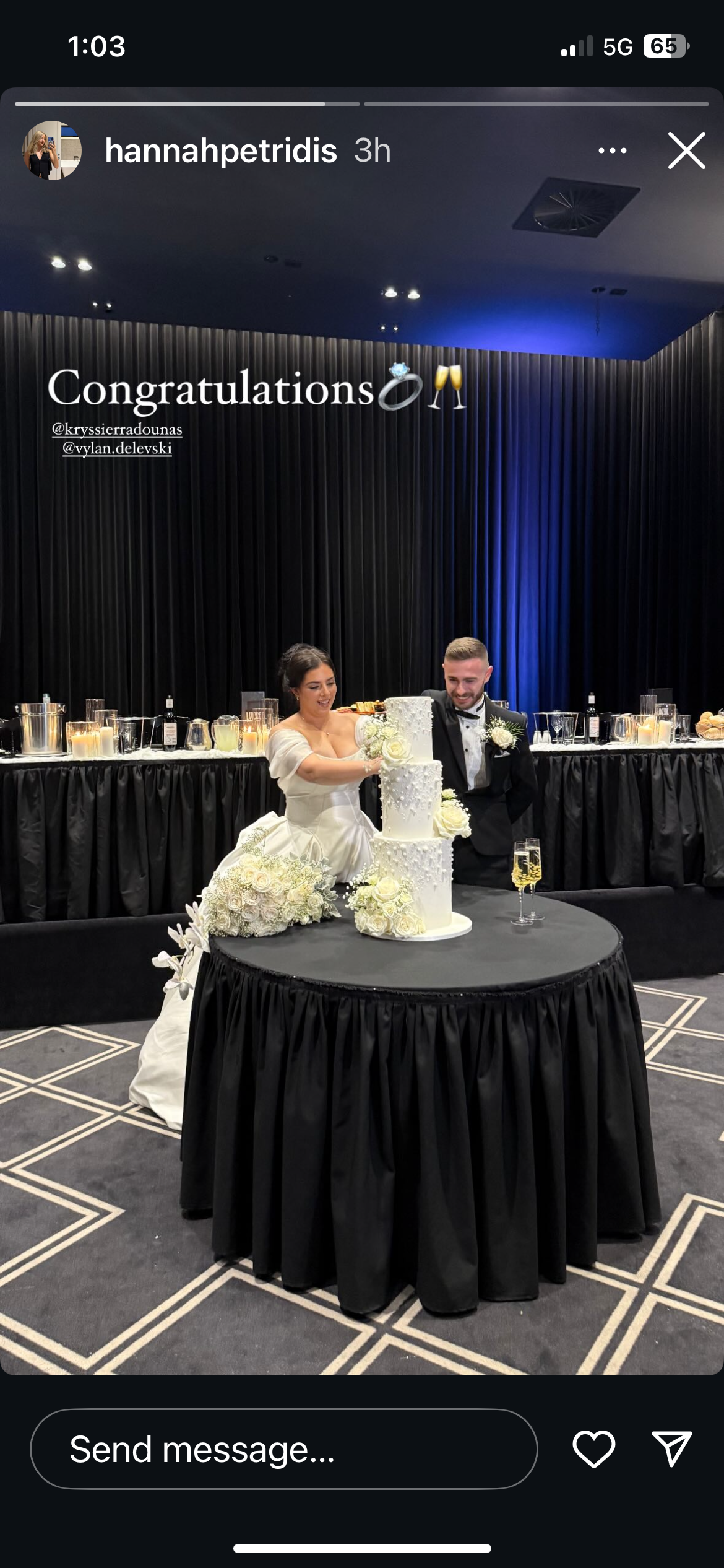 A bride and groom cutting a wedding cake at their reception, with a decorated table and congratulatory message on a black backdrop.