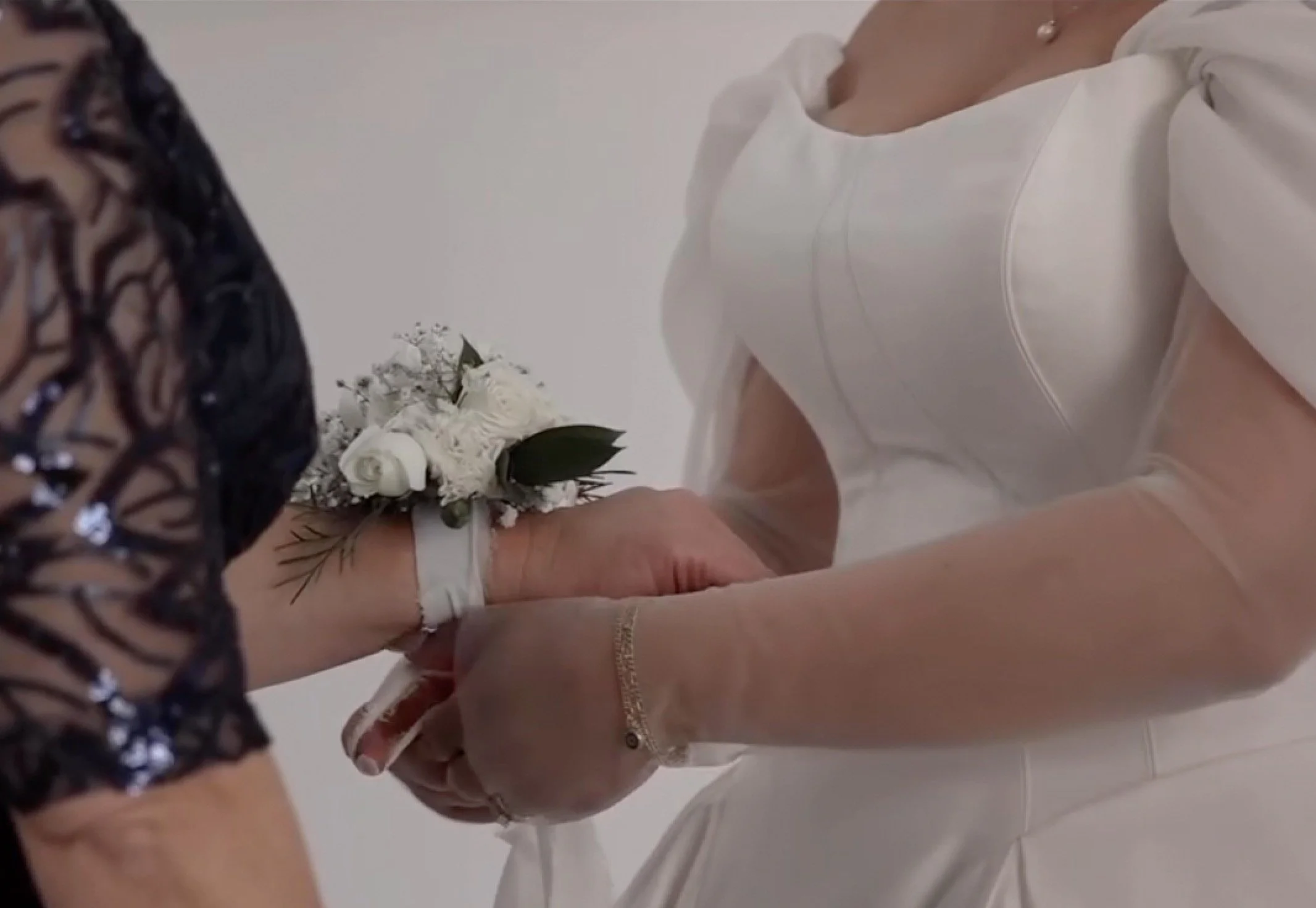 A bride is holding hands with another person while exchanging wedding vows, with a bouquet of white flowers in the background.