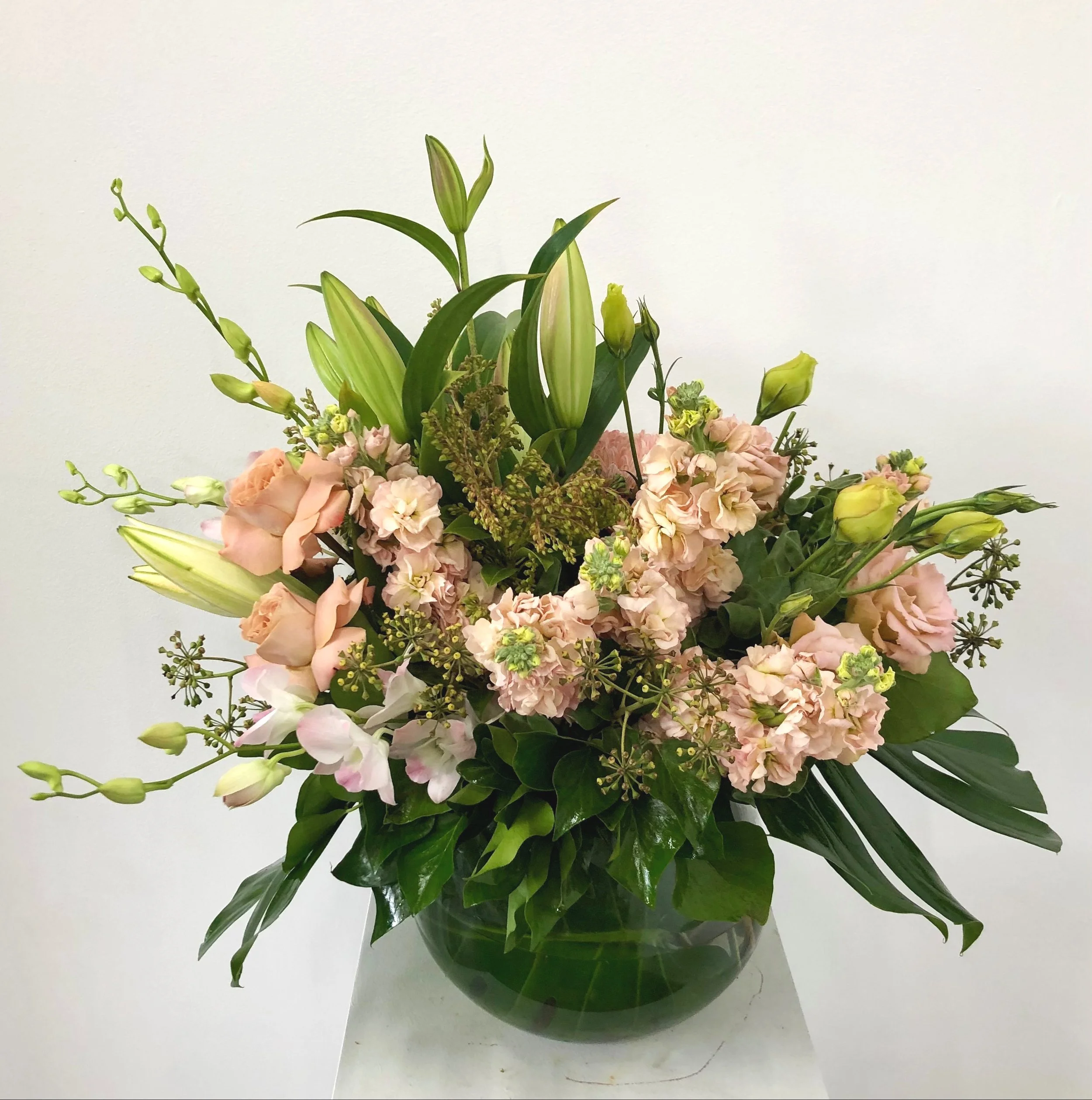A bouquet of pink lilies, roses, and greenery in a glass vase against a plain white background.