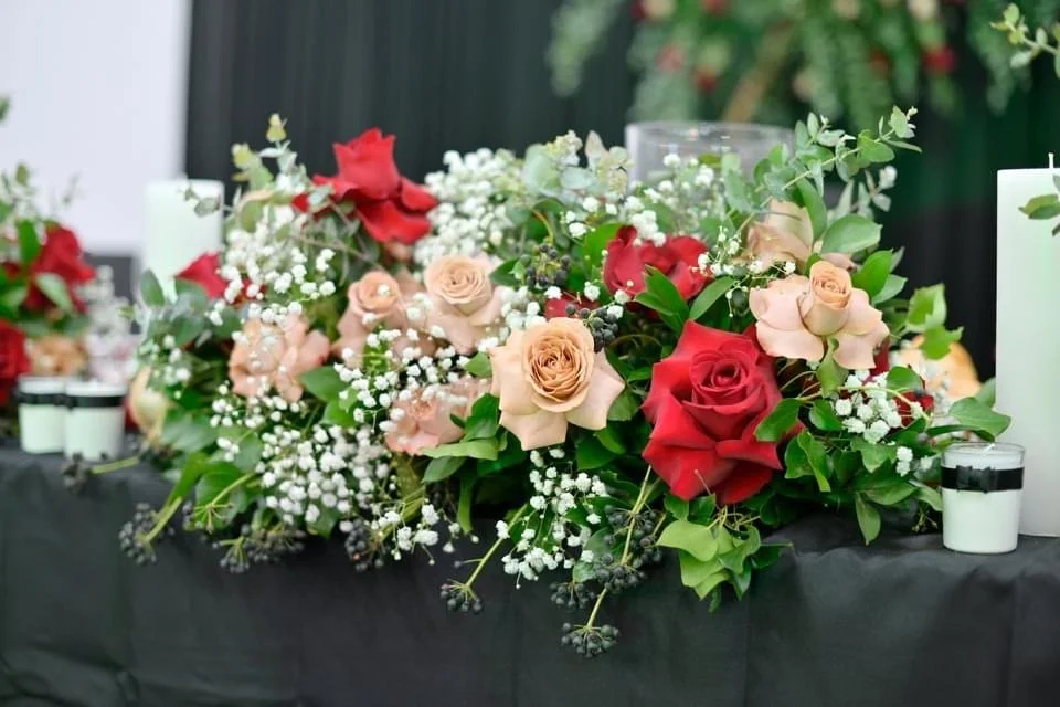 Floral centerpiece with red, pink, and peach roses, white baby's breath, and green foliage on a black tablecloth at a formal event.