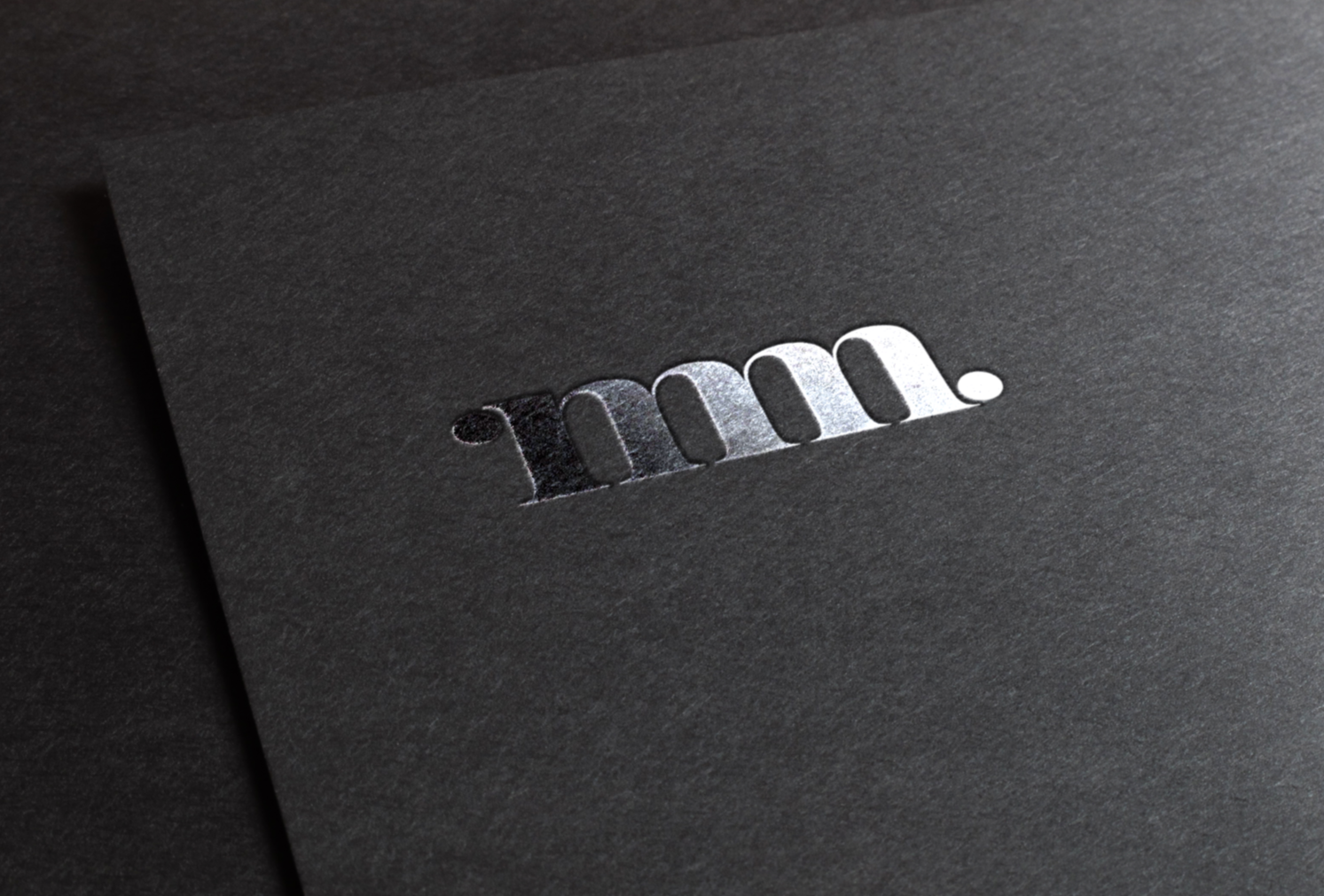 Close-up of a black surface with a metallic embossed logo that reads "m.m." in white.