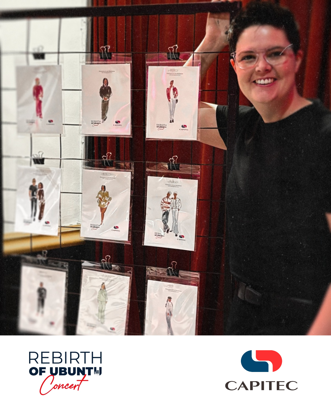A smiling person with short dark hair and glasses taking a mirror selfie in front of a display of various fashion illustrations clipped to a wire grid. The display promotes the 'Rebirth of Ubuntu' concert by Capitec.