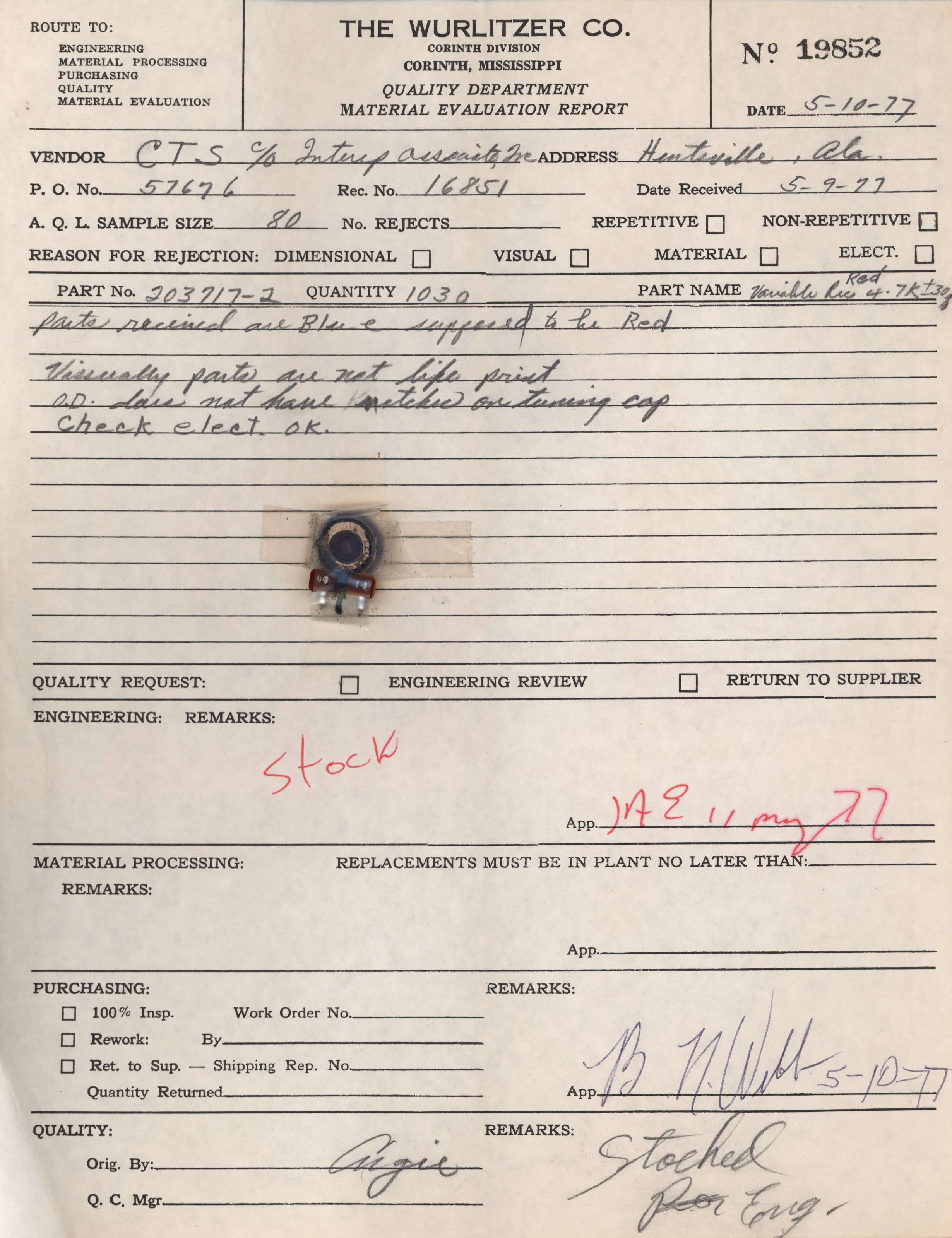 A detailed material evaluation report form from The Wurlitzer Co., Corinth Division, dated May 10, 1977. It includes handwritten notes, signatures, and a small electronic component below the paper, with some parts of the sheet torn or damaged.
