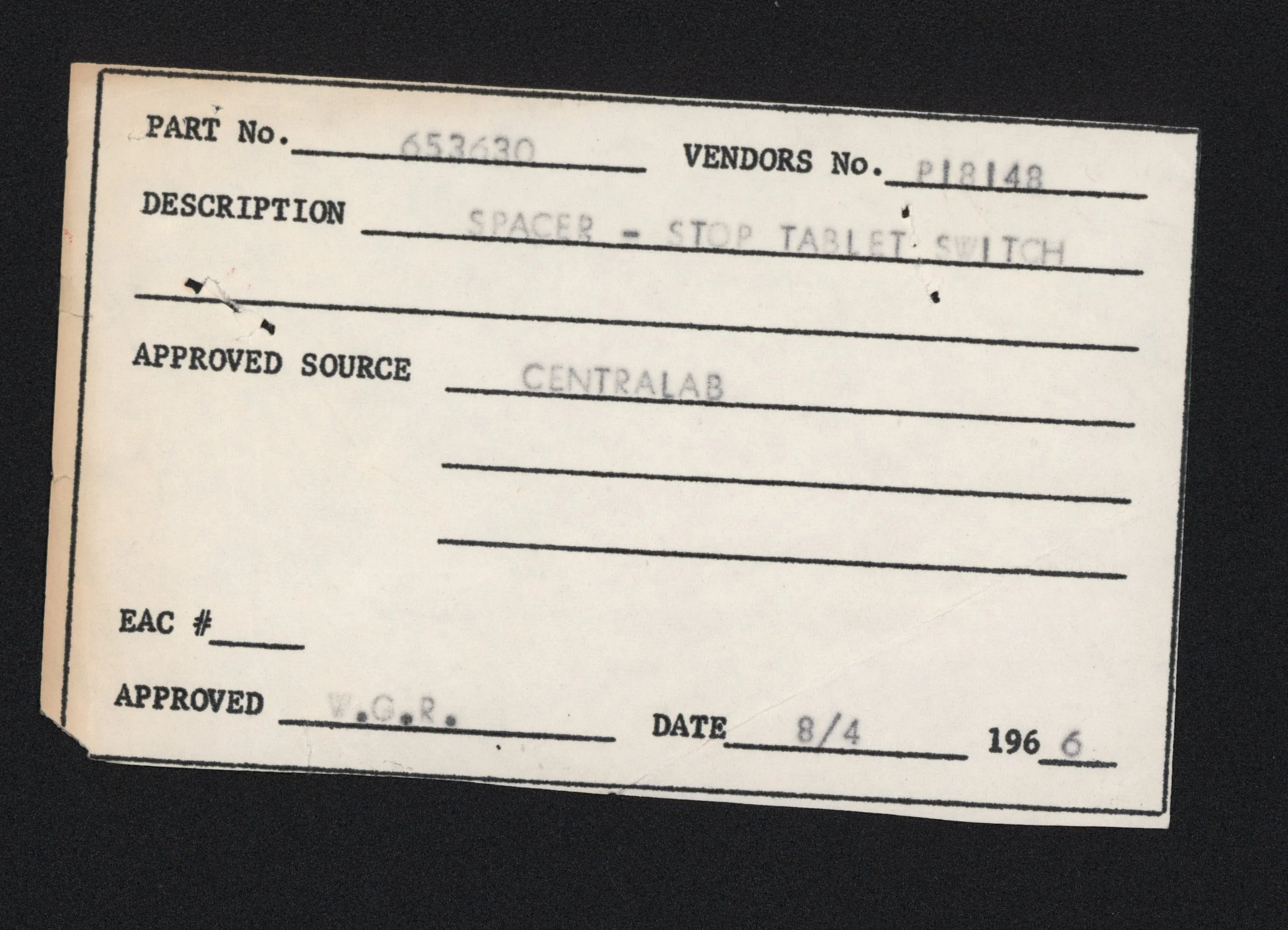 Close-up of a vintage-style document with typed and handwritten information, including part number, vendor number, description, approval source, and date, against a black background.