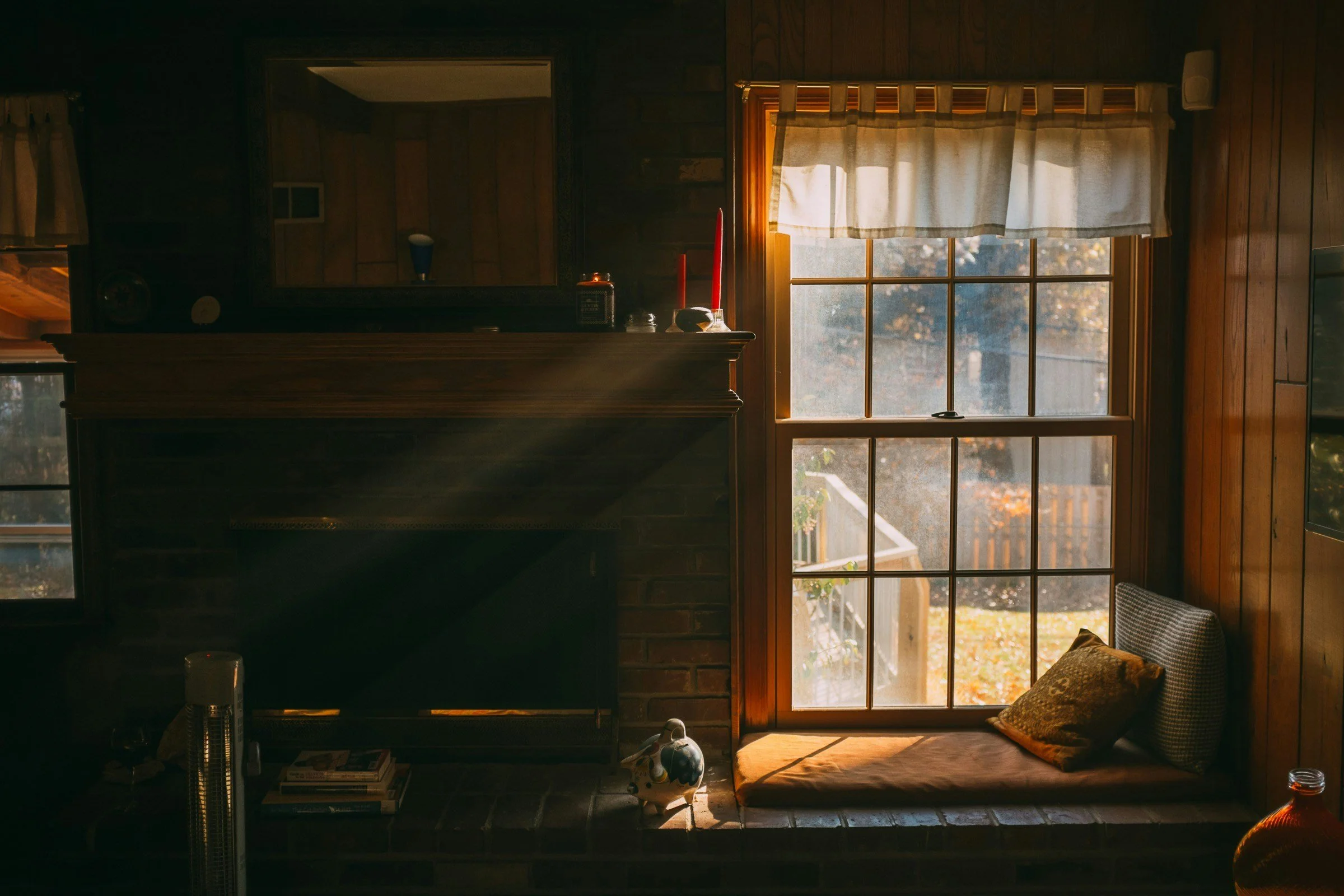 Sunlight streaming through a window onto a cozy window seat with a pillow inside a wooden-paneled room.