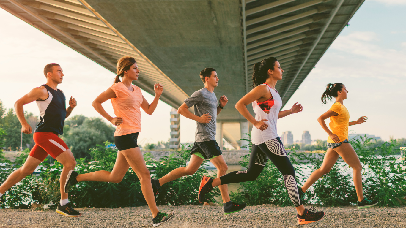 Groupe de cinq personnes en tenue de sport courant en plein air sous un pont suspendu.