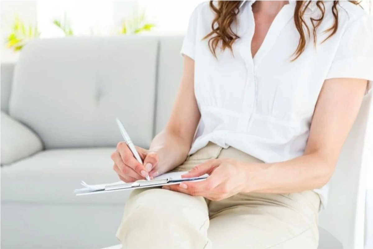 Therapist writing notes during a session in a calm, neutral office, representing trust, professionalism, and emotional safety in modern therapy websites.