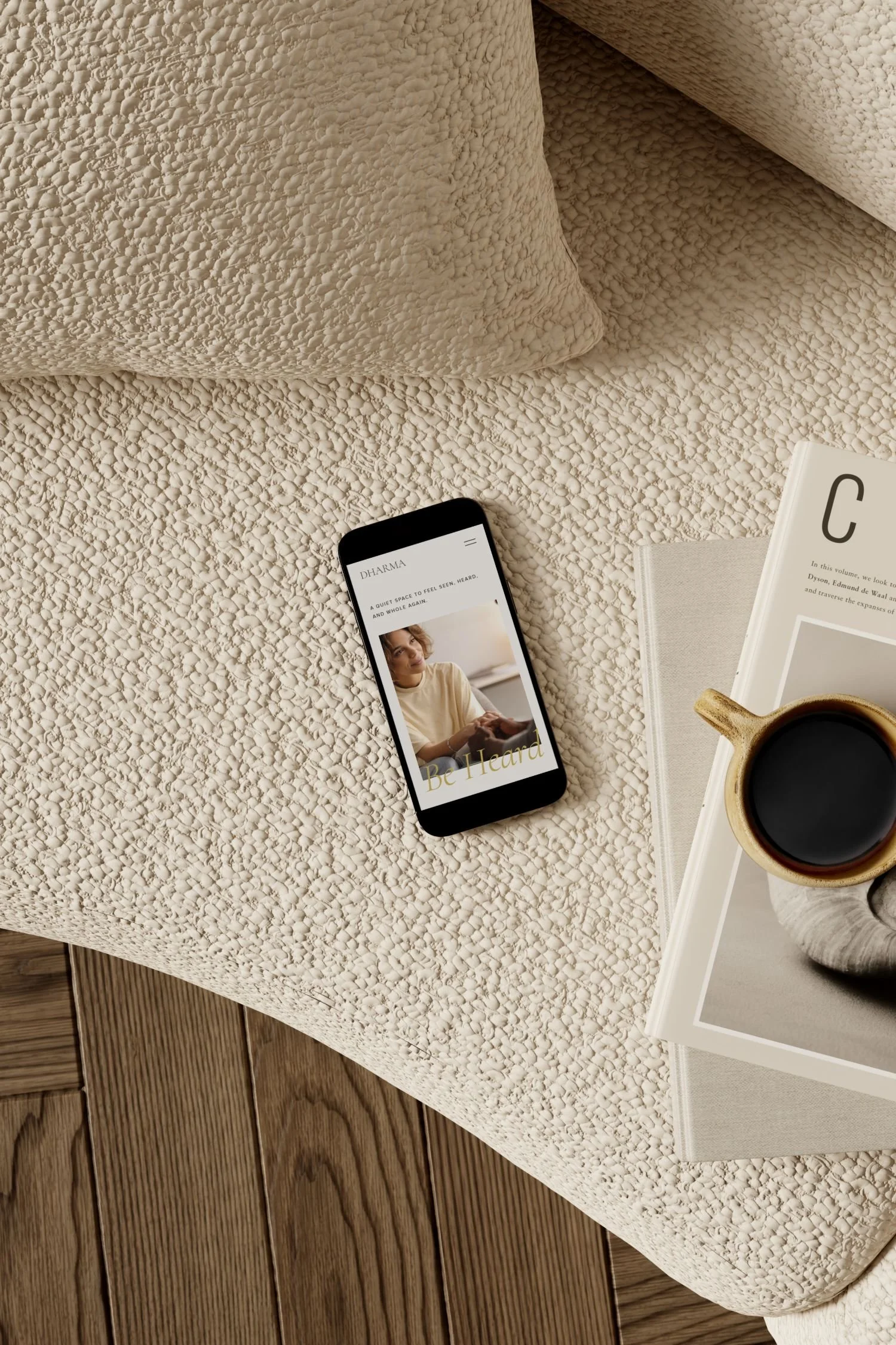 A beige textured bed with a smartphone portraying Dharma mobile version, a magazine, and a cup of coffee placed on it.