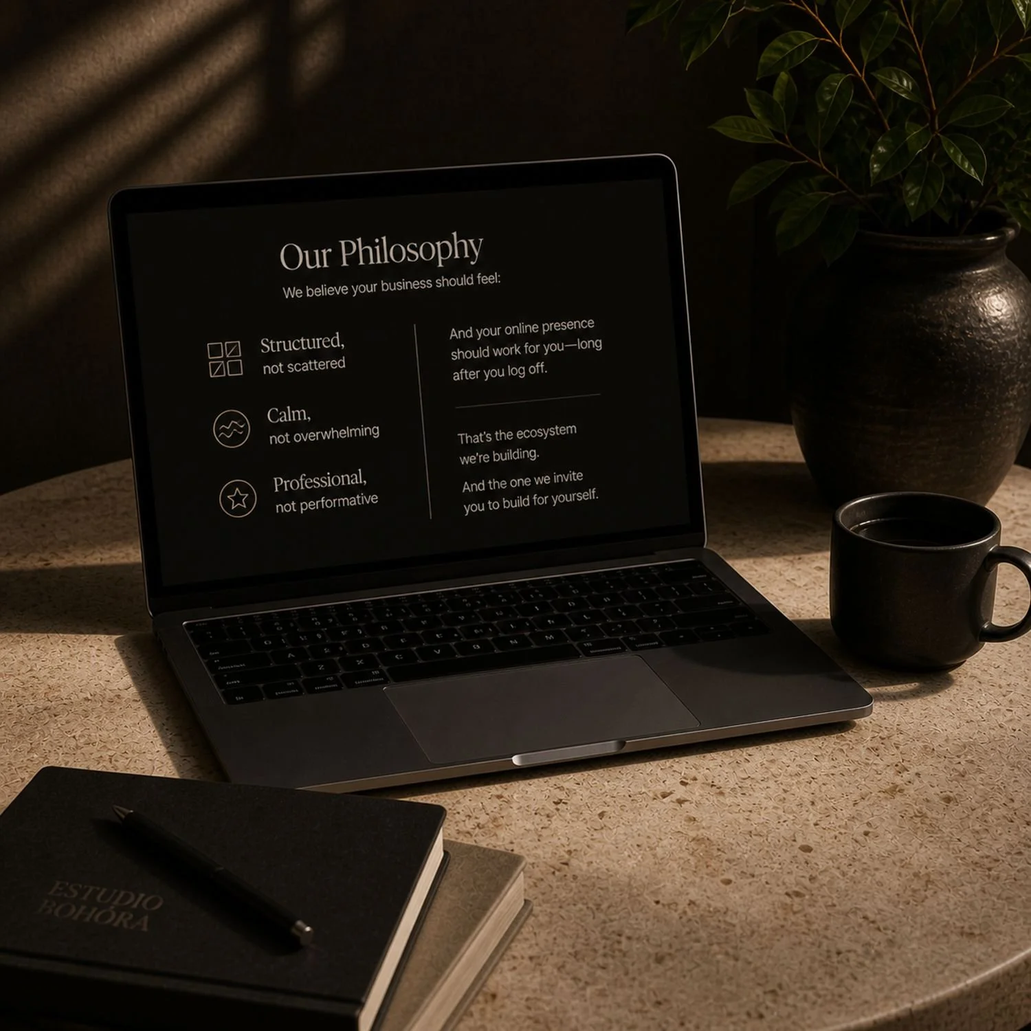 A laptop on a textured beige desk displaying a presentation titled 'Our Philosophy' with three bullet points. Next to the laptop is a black coffee mug, a potted plant, and a notebook with a pen on top.
