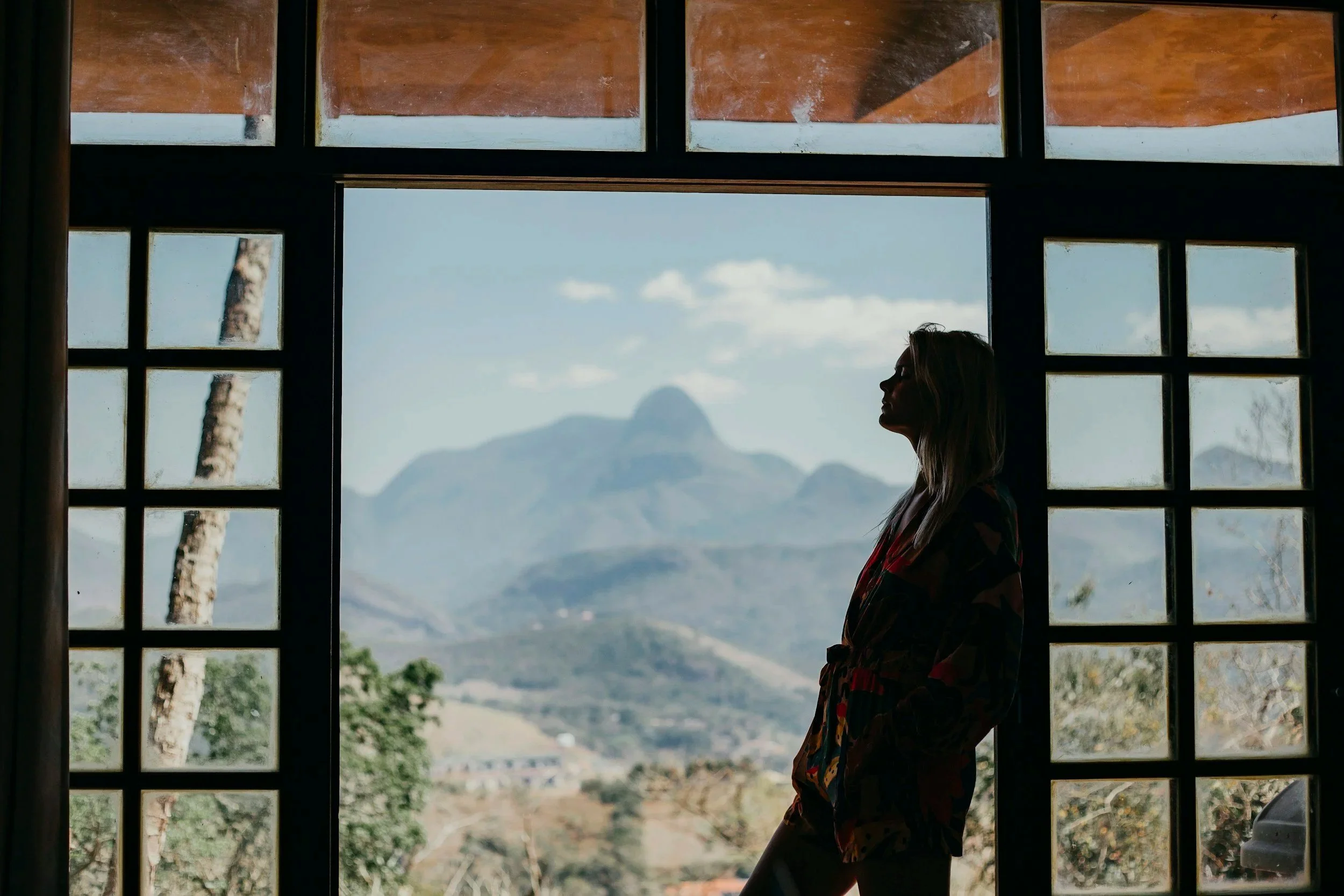 Woman standing calmly by a window with mountains in the background, representing acupuncture for anxiety and nervous system regulation