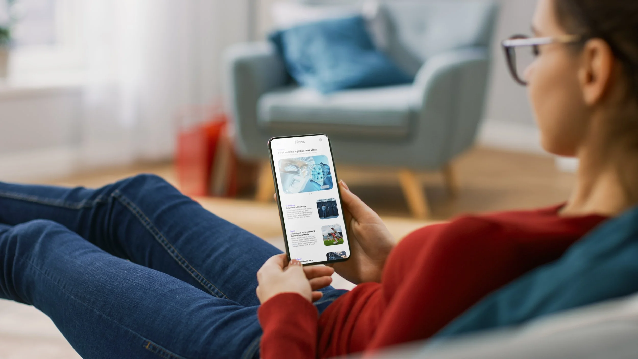 Person som ligger på en sofa og leser nyheter på mobiltelefon.