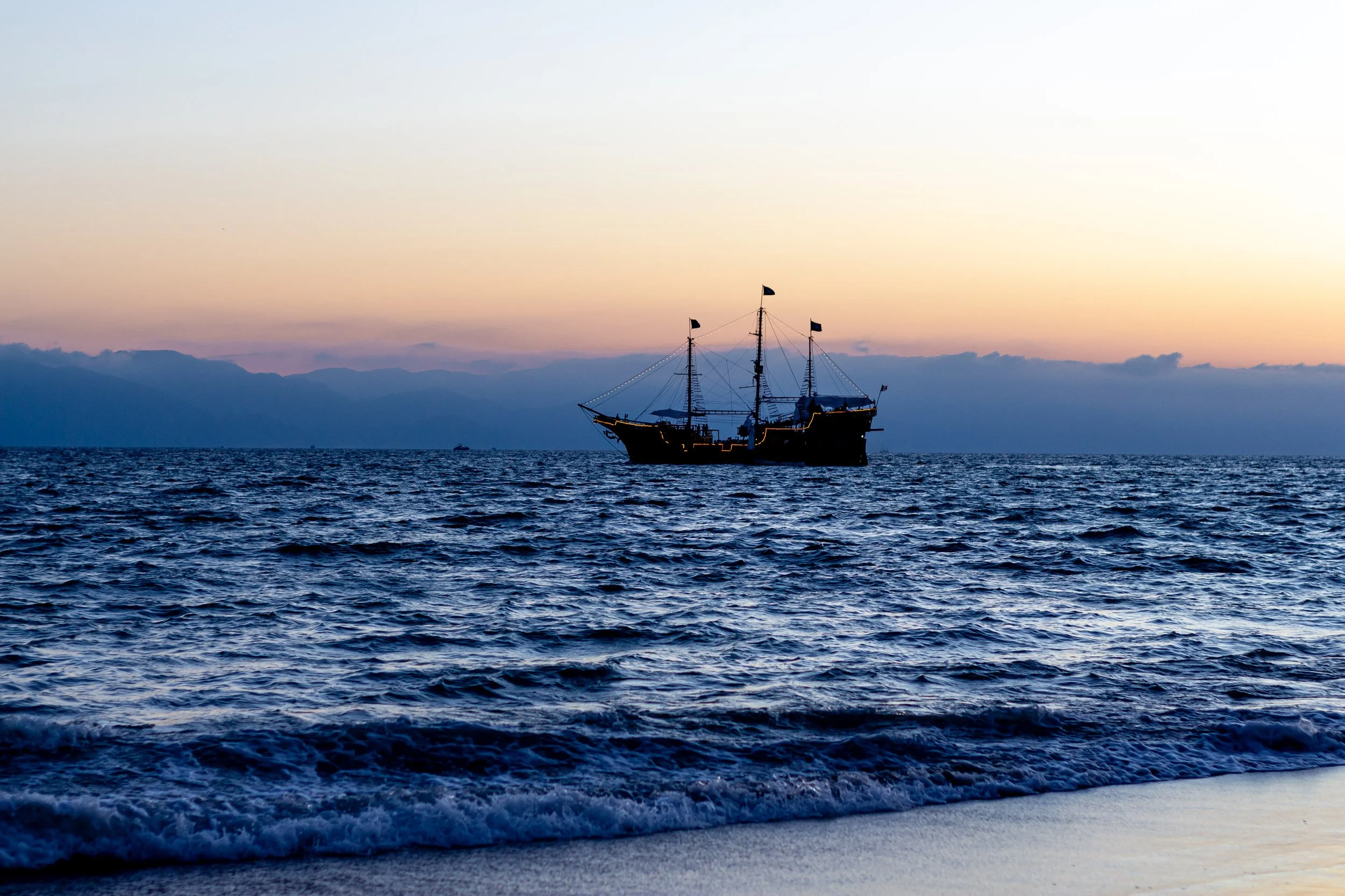 A sailboat on the ocean during sunset with mountains in the background.