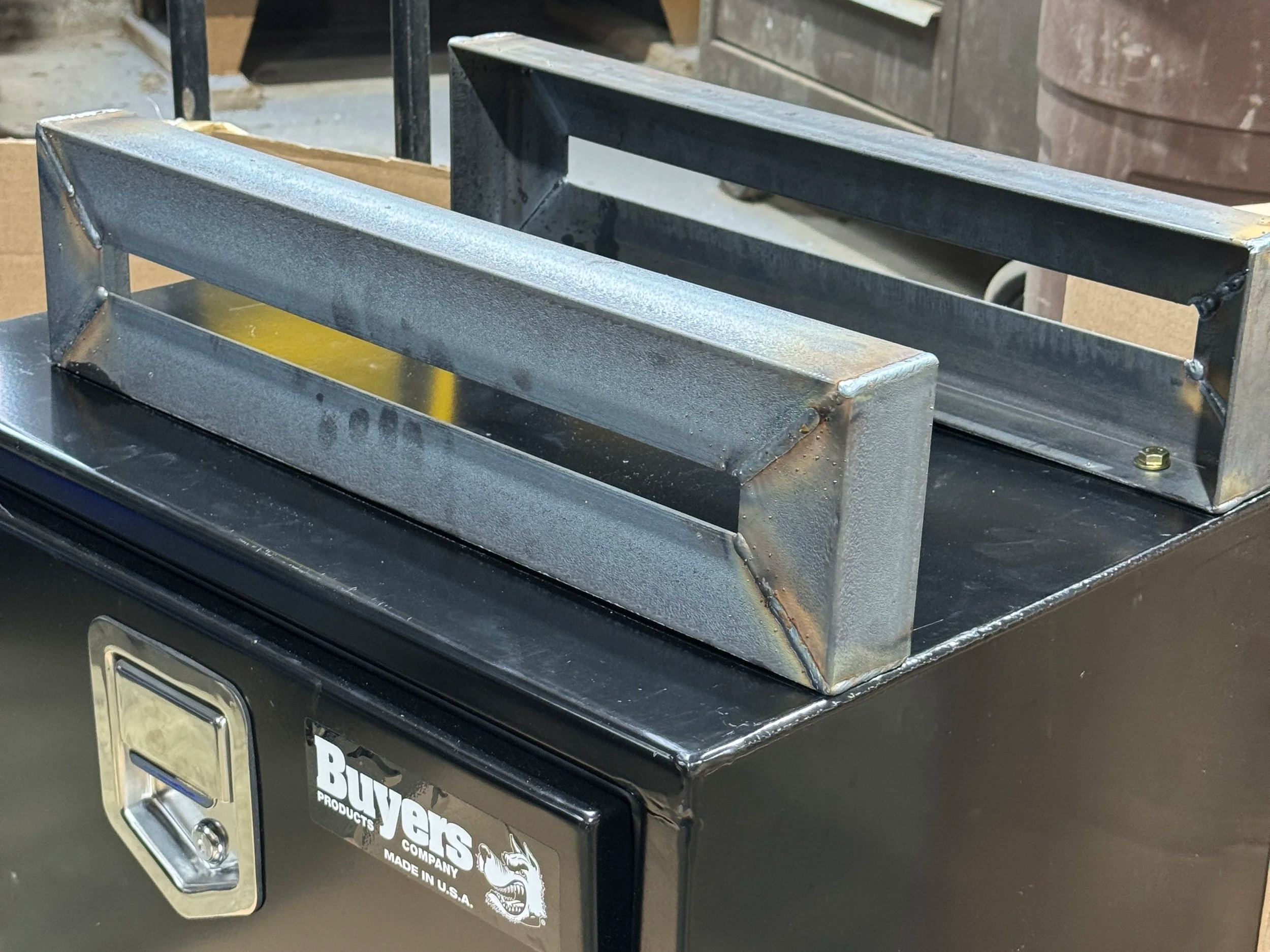 Close-up of welded steel angle mounts supporting underbody toolbox on flatbed truck