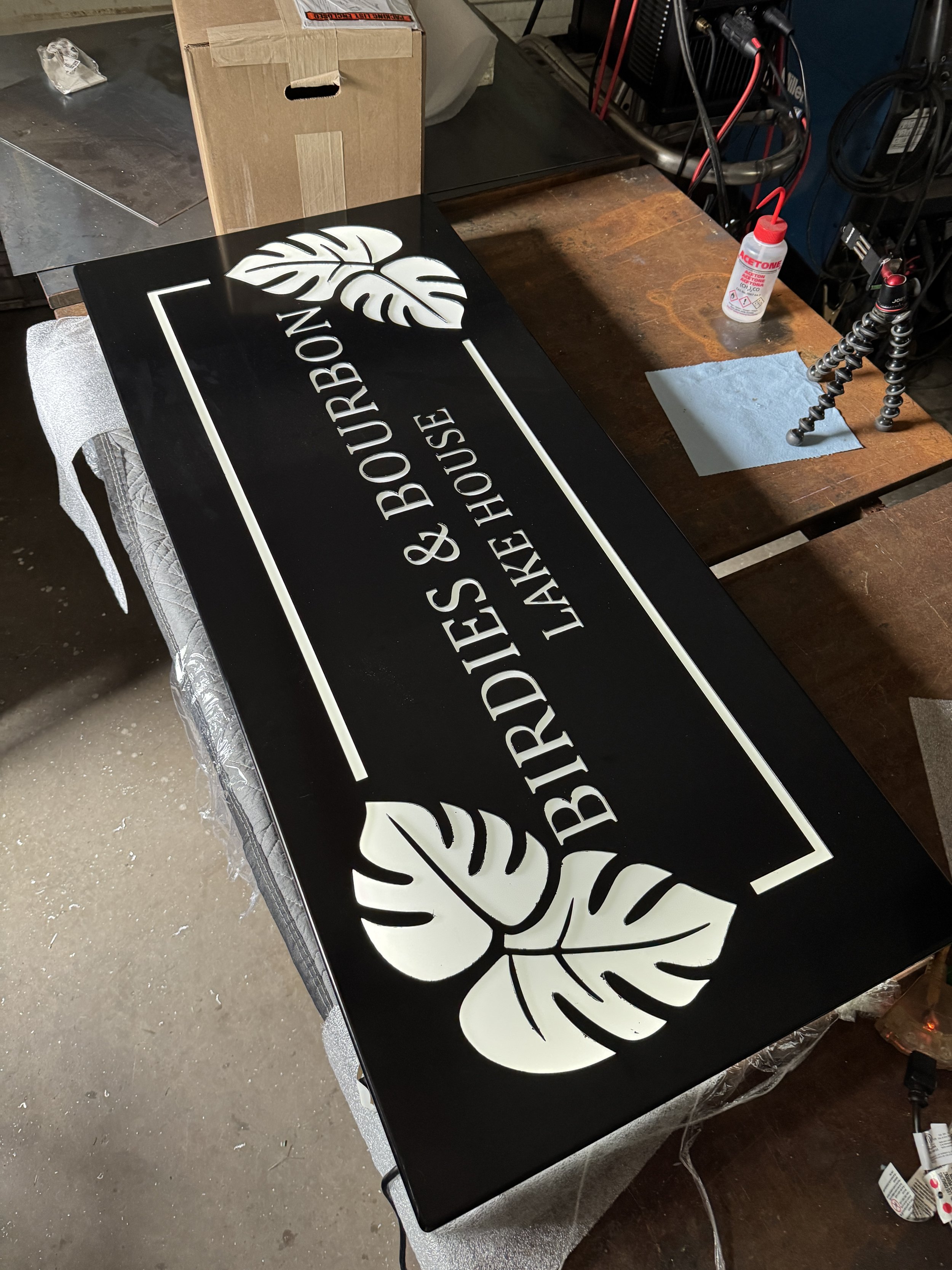 Black powder-coated architectural metal sign with white acrylic backing and custom-cut lettering