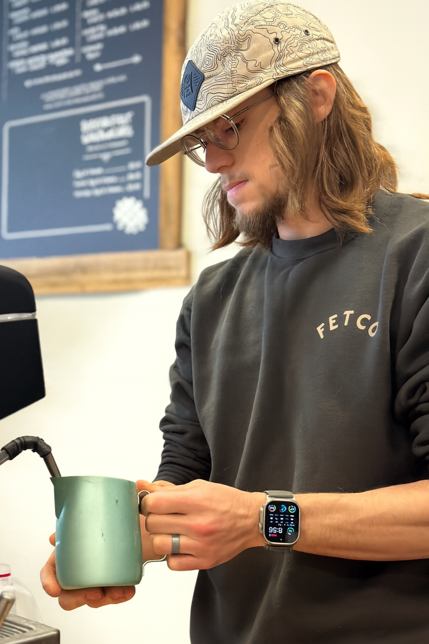 A man smiling and holding a large fish on a boat during a fishing trip, with a bridge over water in the background.