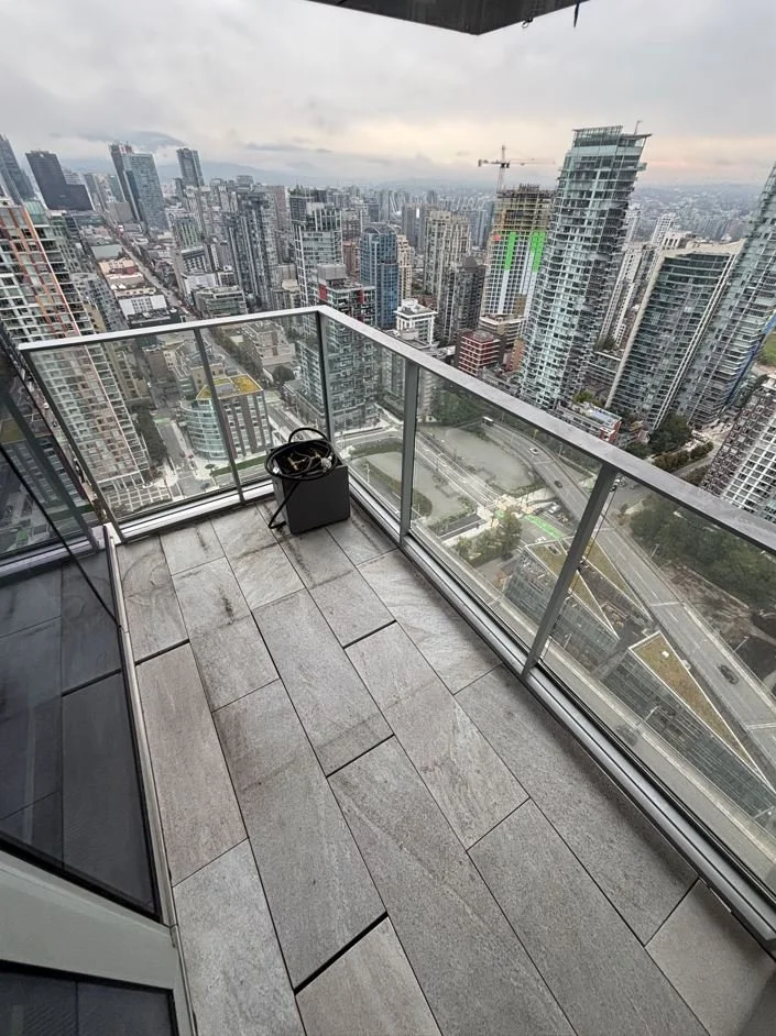 View from a high-rise balcony overlooking a cityscape with numerous modern skyscrapers and construction cranes on a cloudy day.