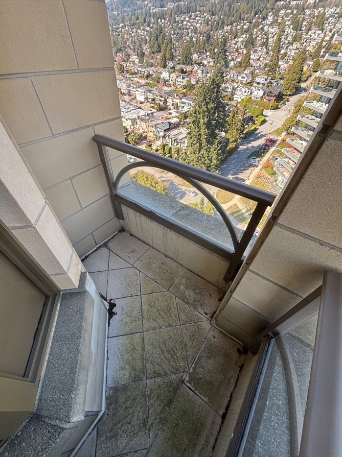 Small balcony with a metal railing, overlooking a city with many houses and trees, high above the street level.
