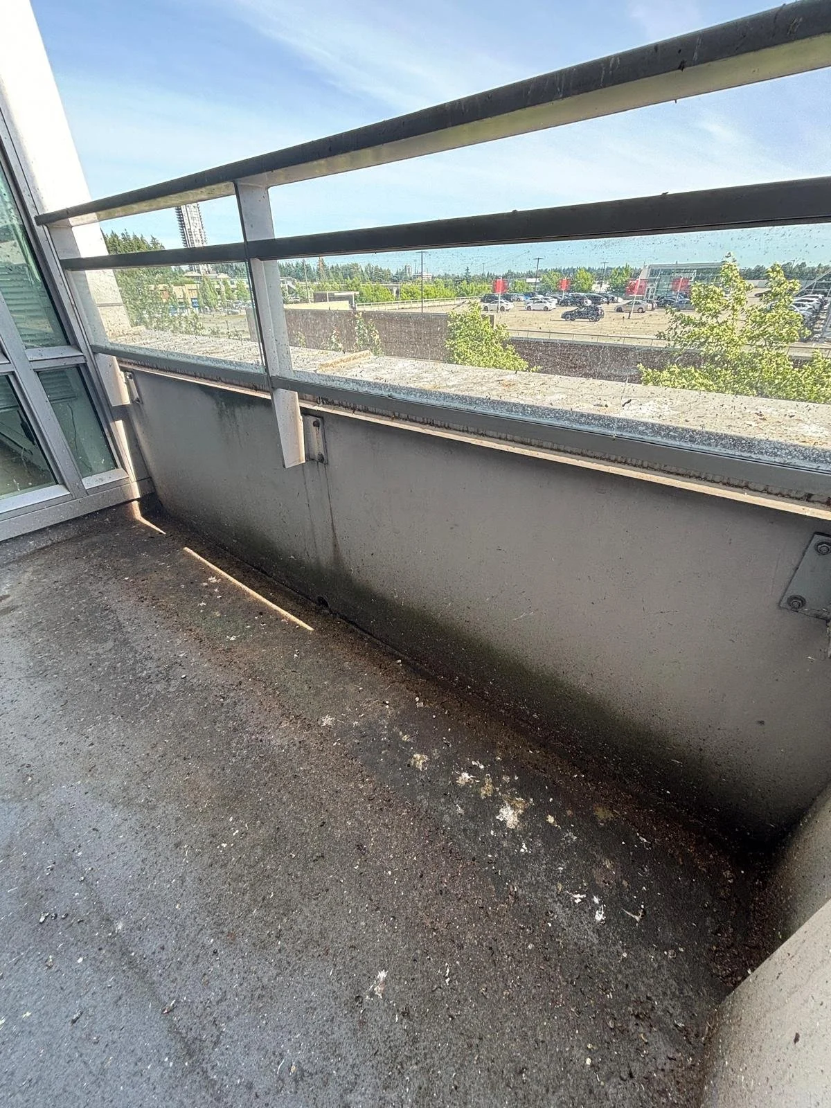 Balcony with gravel floor, metal railing, and a view of a parking lot and trees under a clear blue sky.