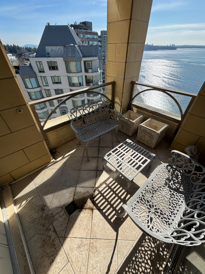 Balcony with wrought iron furniture overlooking water and cityscape with buildings in the background.