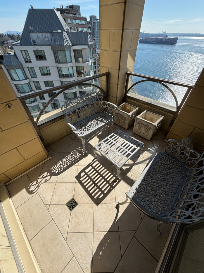 Small balcony with metal chairs, empty planters, and a view of water with a ship in the distance.