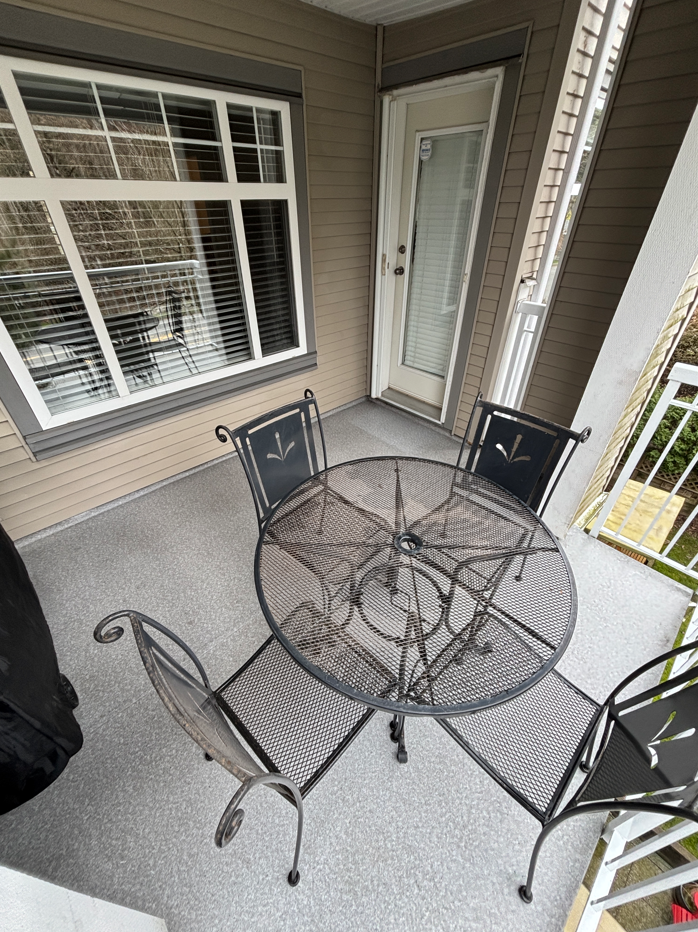 Outdoor patio with a metal table and four matching chairs, a window with blinds, a door with a glass panel, and a railing on the right side.