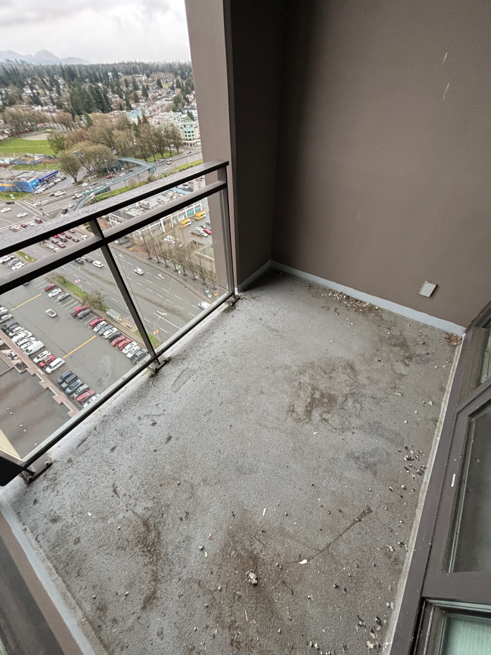 Empty balcony with dirt and debris, overlooking a parking lot and a park in an urban area.