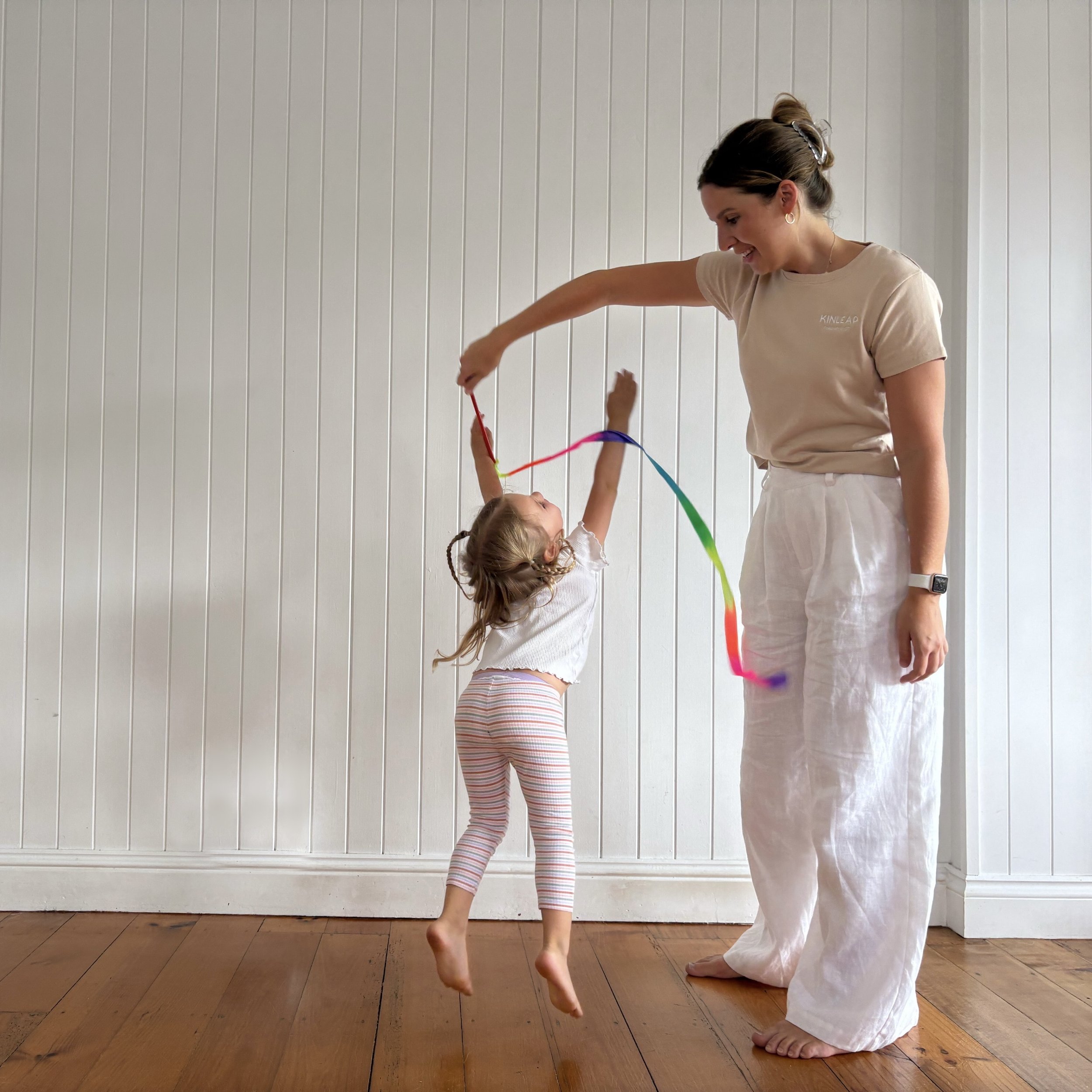Kinleap paediatric Occupational Therapist supporting a young girl with gross motor and cognitive skill development using a rainbow ribbon indoors on the Sunshine Coast.