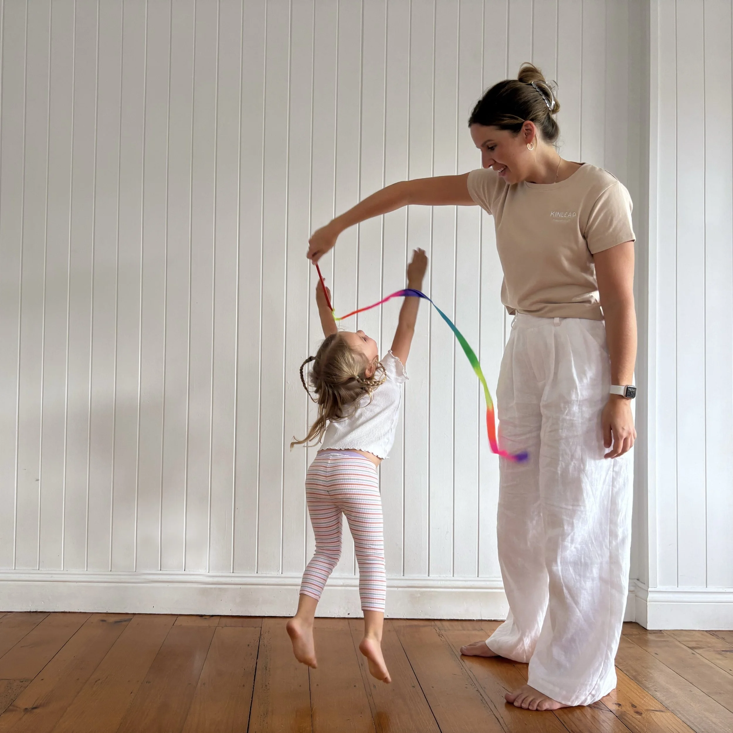 Paediatric occupational therapist playing ribbon twirl game with a child jumping through the ribbon during a clinic session in Birtinya, Sunshine Coast