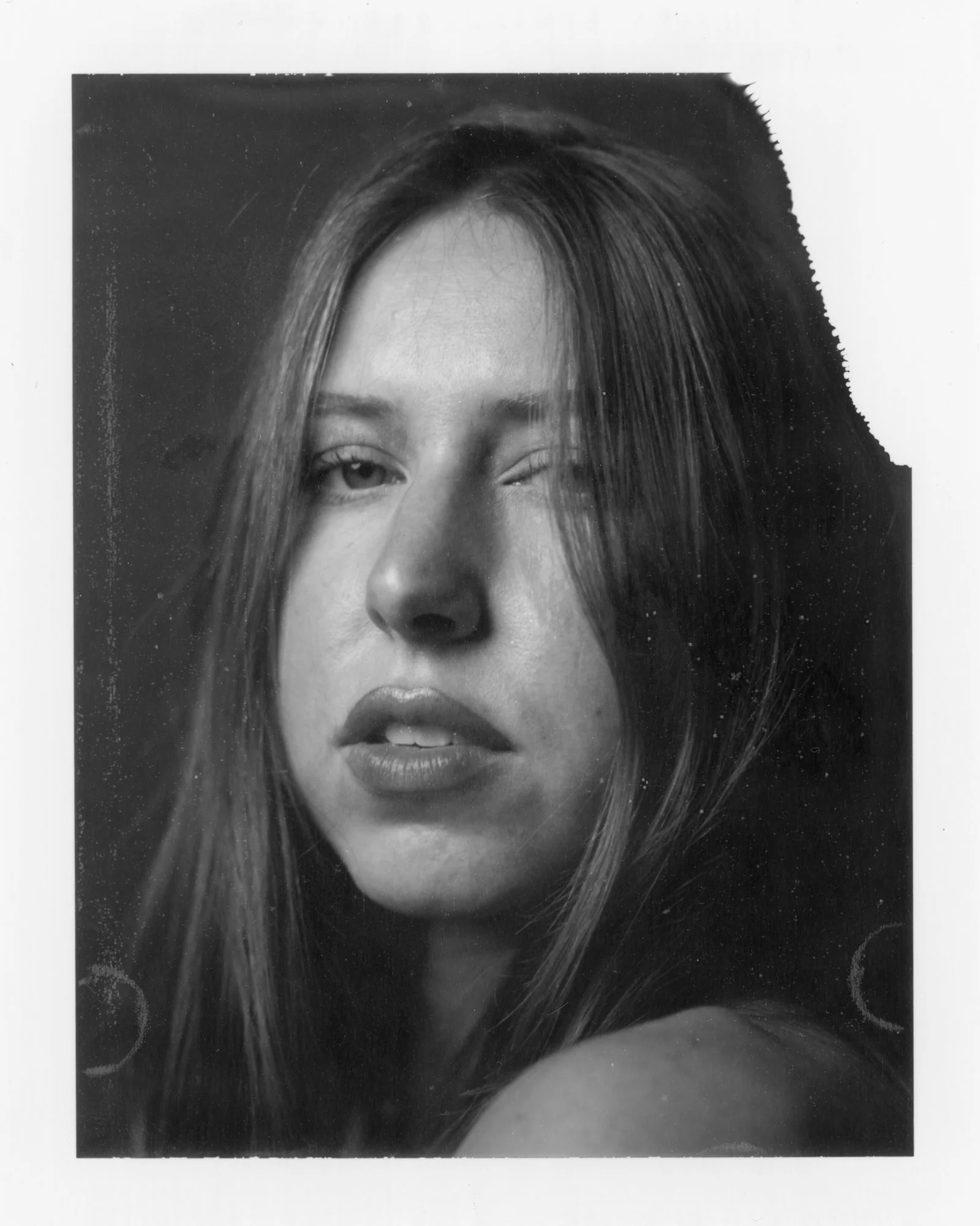 Black and white portrait of a woman with one eye slightly open and lips parted, with long straight hair partially covering her face.