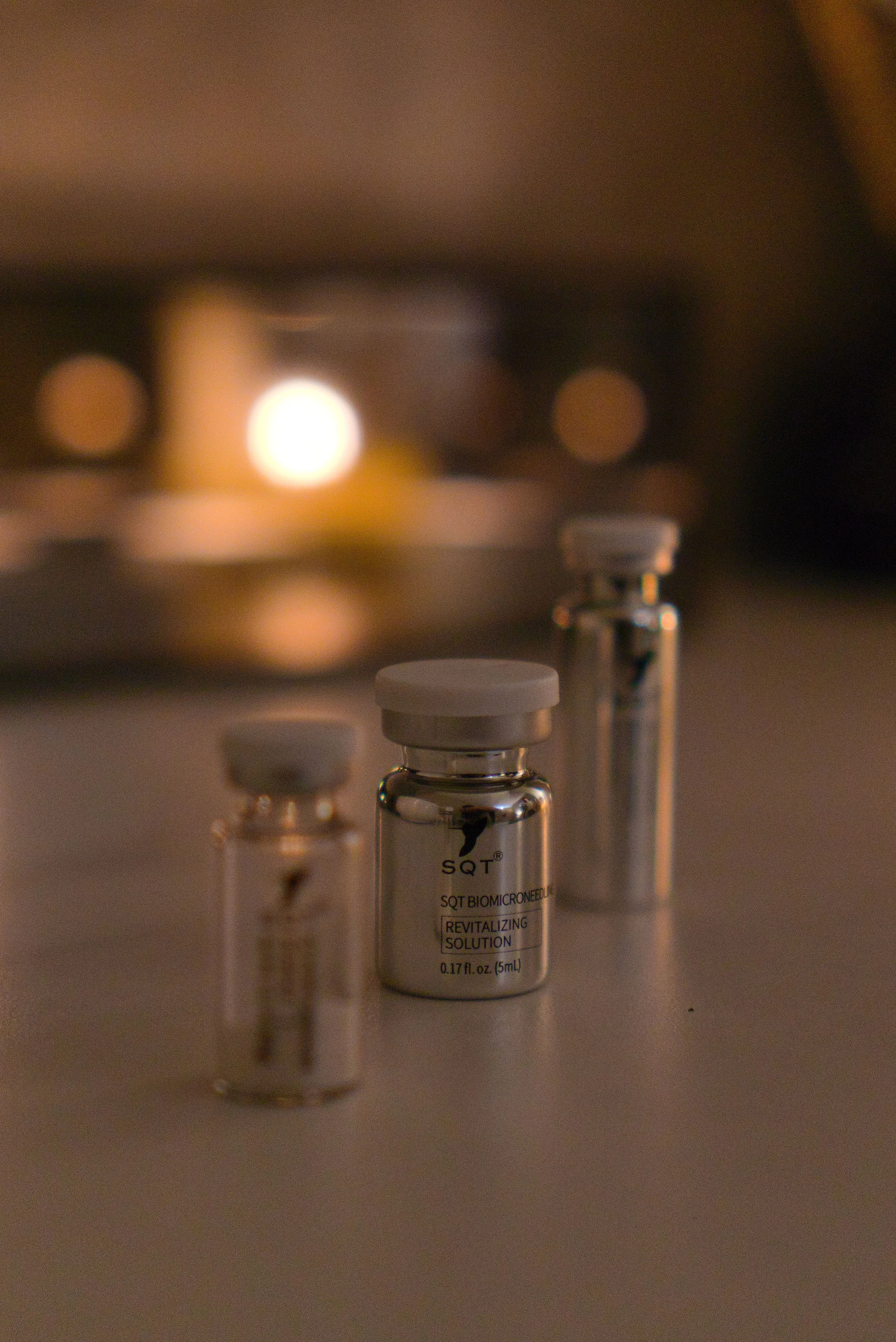 Three small bottles labeled 'Revitalizing Solution' and 'SQ T Biomicroneedle' on a flat surface, with a blurred background of warm lighting.