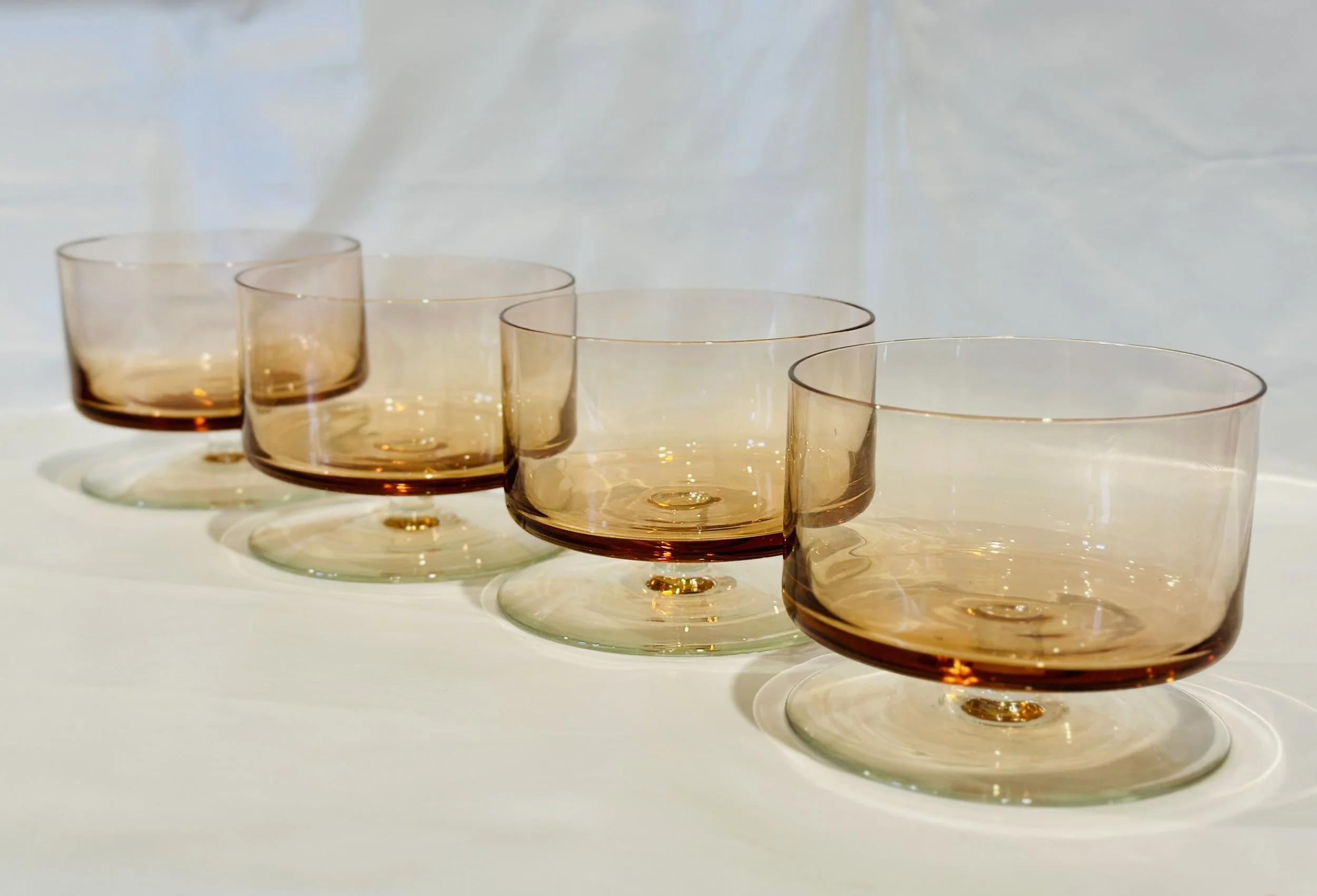 Six amber-tinted drinking glasses arranged in a row on a white surface with a white background. Available in the Curated by Curtis online Vintage Store. 