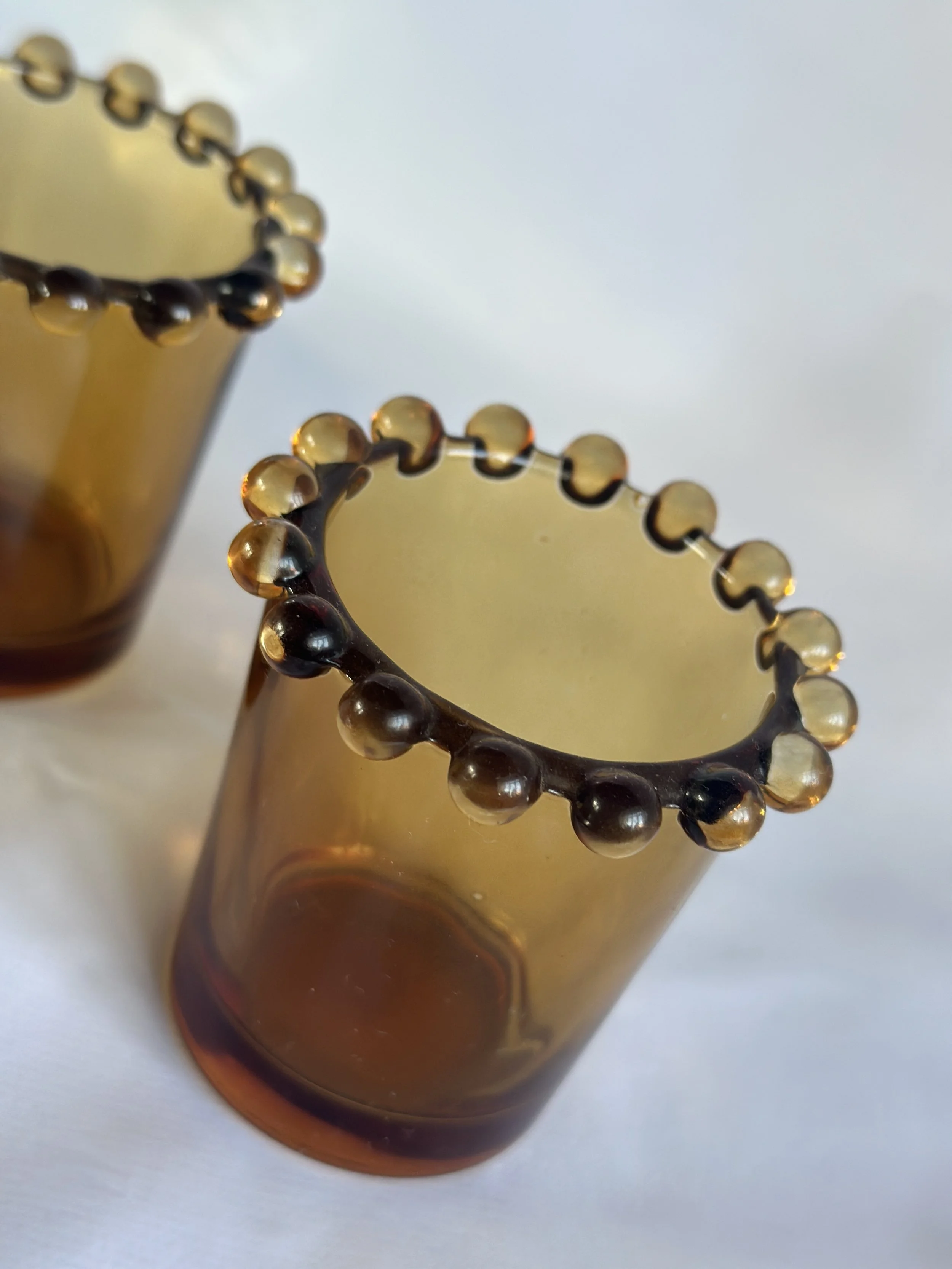 Close-up of a decorative amber-colored glass vase and a matching glass bracelet with dark beads on the edge, set against a white background. Available in the Curated by Curtis online Vintage Store. 