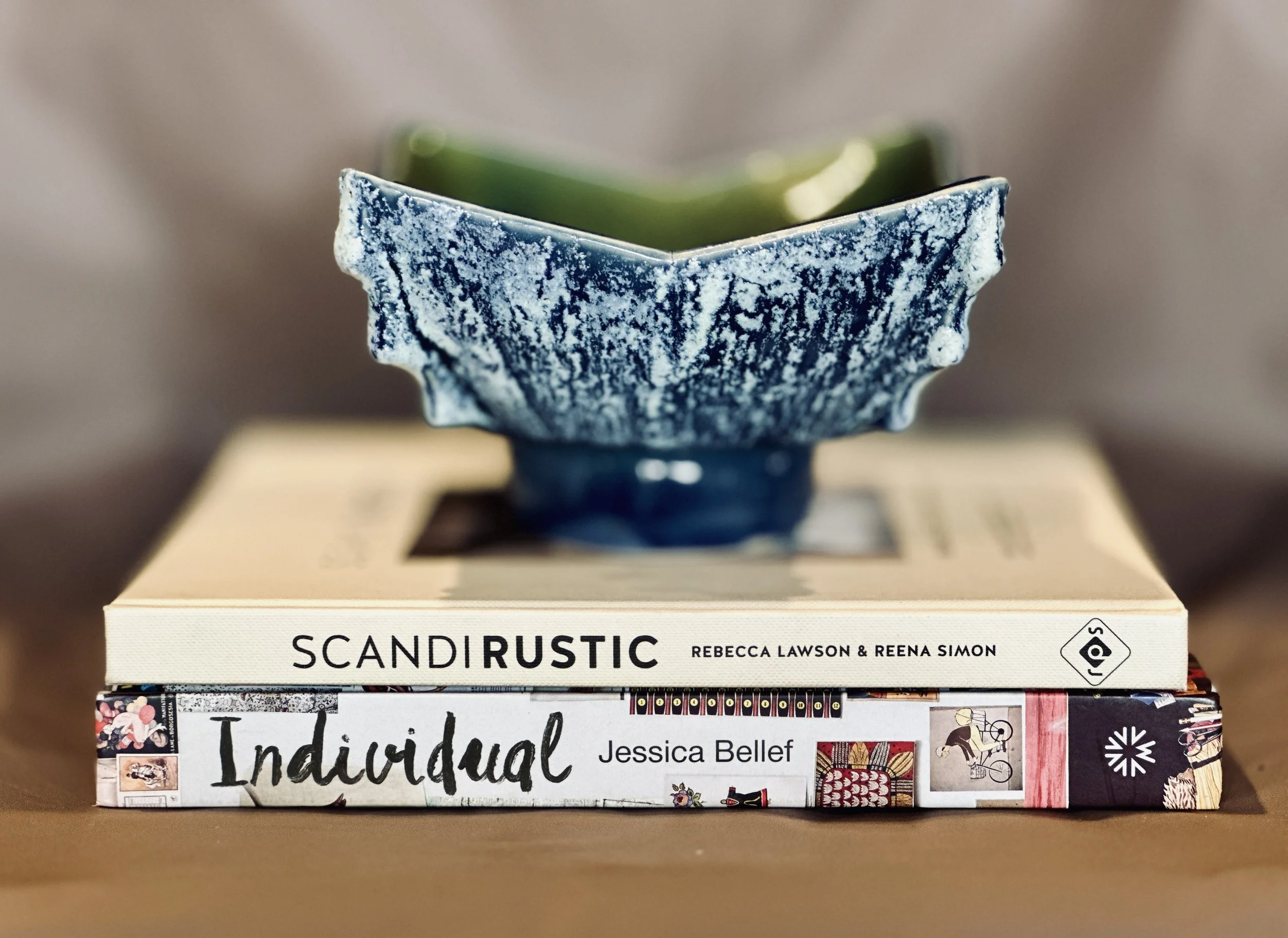 Stack of books with the top one titled 'SCANDI RUSTIC' by Rebecca Lawson & Reena Simon, placed on a table with a blurry background. Available in the Curated by Curtis online Vintage Store. 