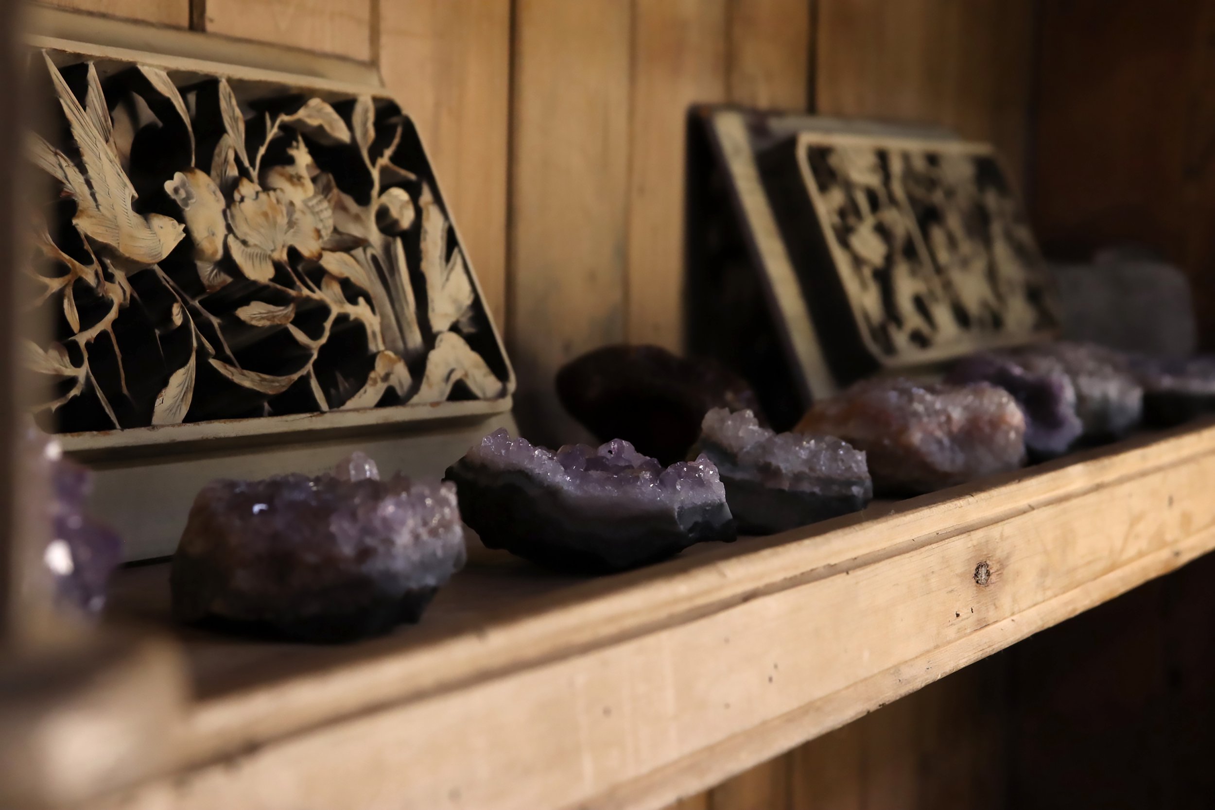 Several amethyst crystal geodes and carved wooden plaques with intricate bird and nature designs on a wooden shelf.
