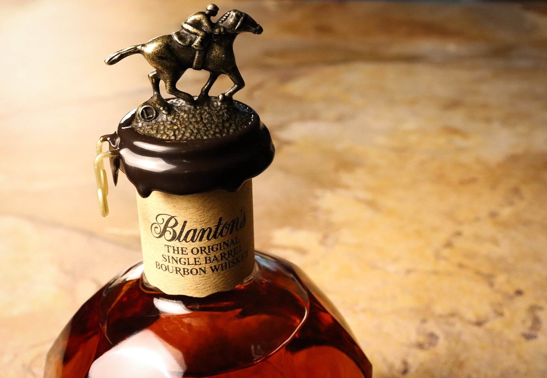 Close-up of a bottle of Blanton's bourbon whiskey with a detailed horse and jockey topper on the cork, on a wooden surface.