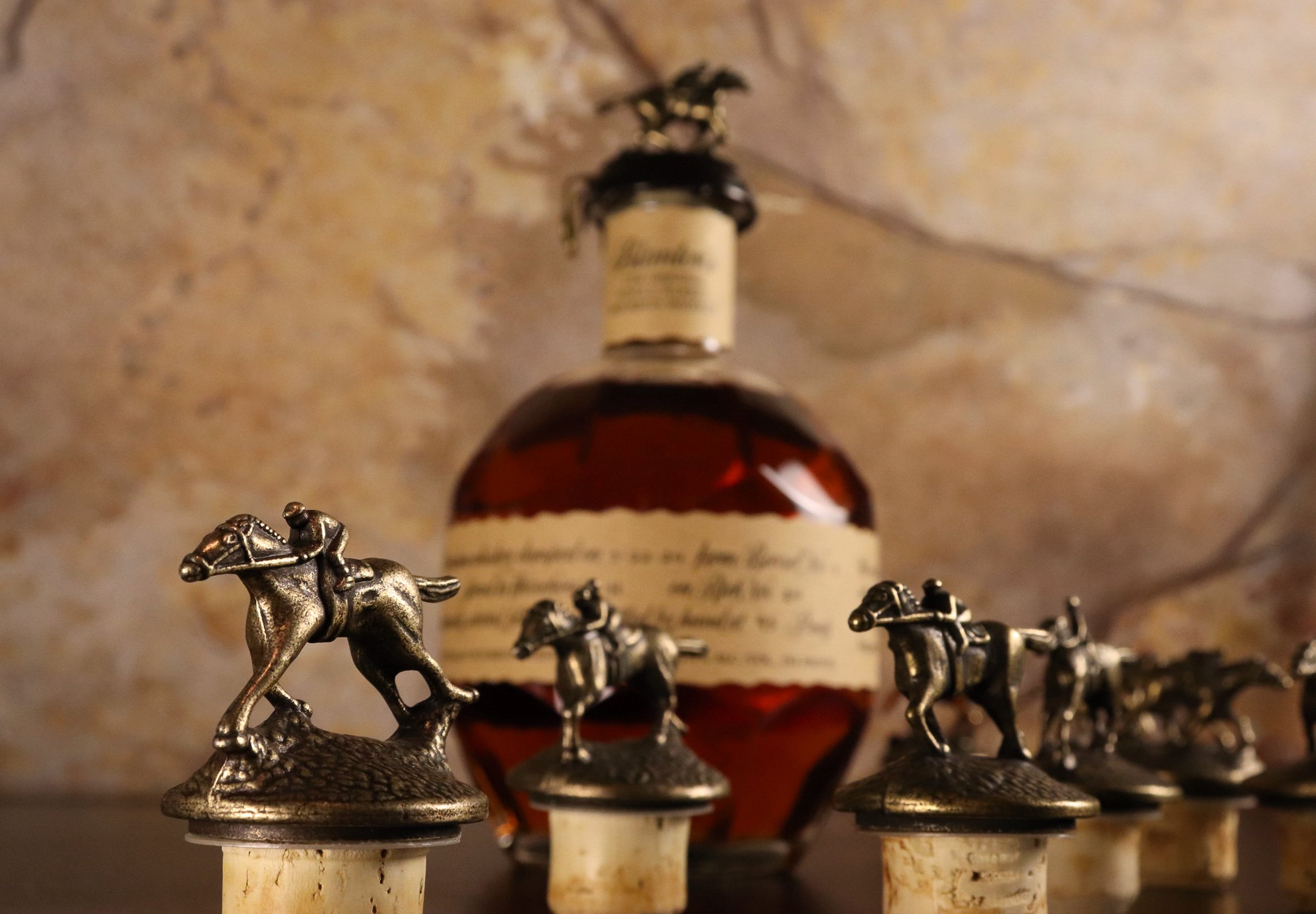 A bowler hat, a bottle of whiskey, and small metal horse figurines on cork bases.