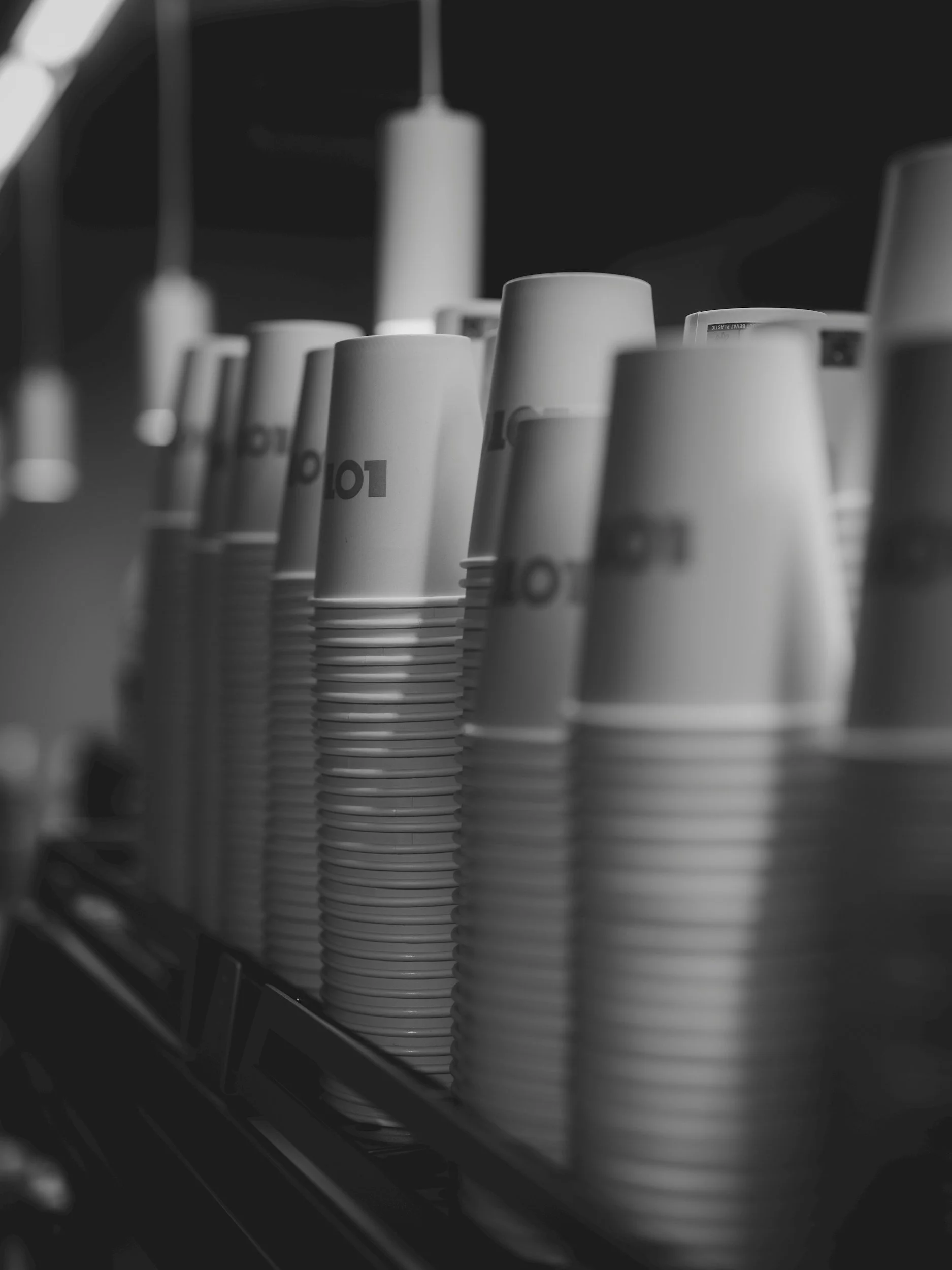 Black and white photo of stacked paper cups on a conveyor belt in a commercial setting.