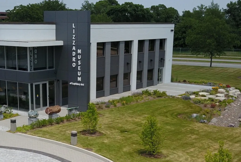 Image is of a 2 story office building in Oak Brook, Illinois, , housing the Lizzadro Museum of Lapidary Art, the corner entry displays name in white letters on a black stone almost two stories high.