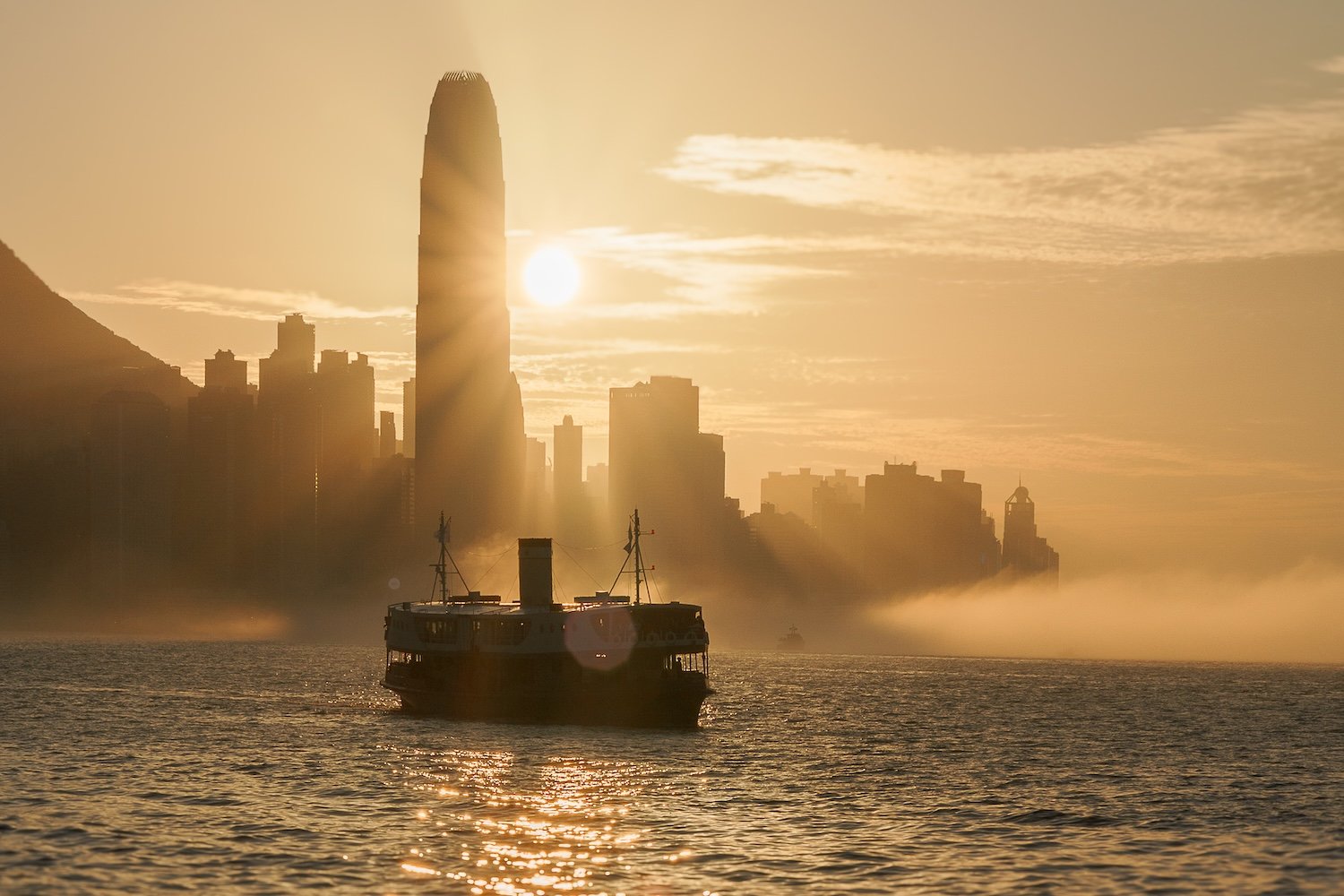 A boat on the water at sunset with a city skyline and foggy haze in the background.