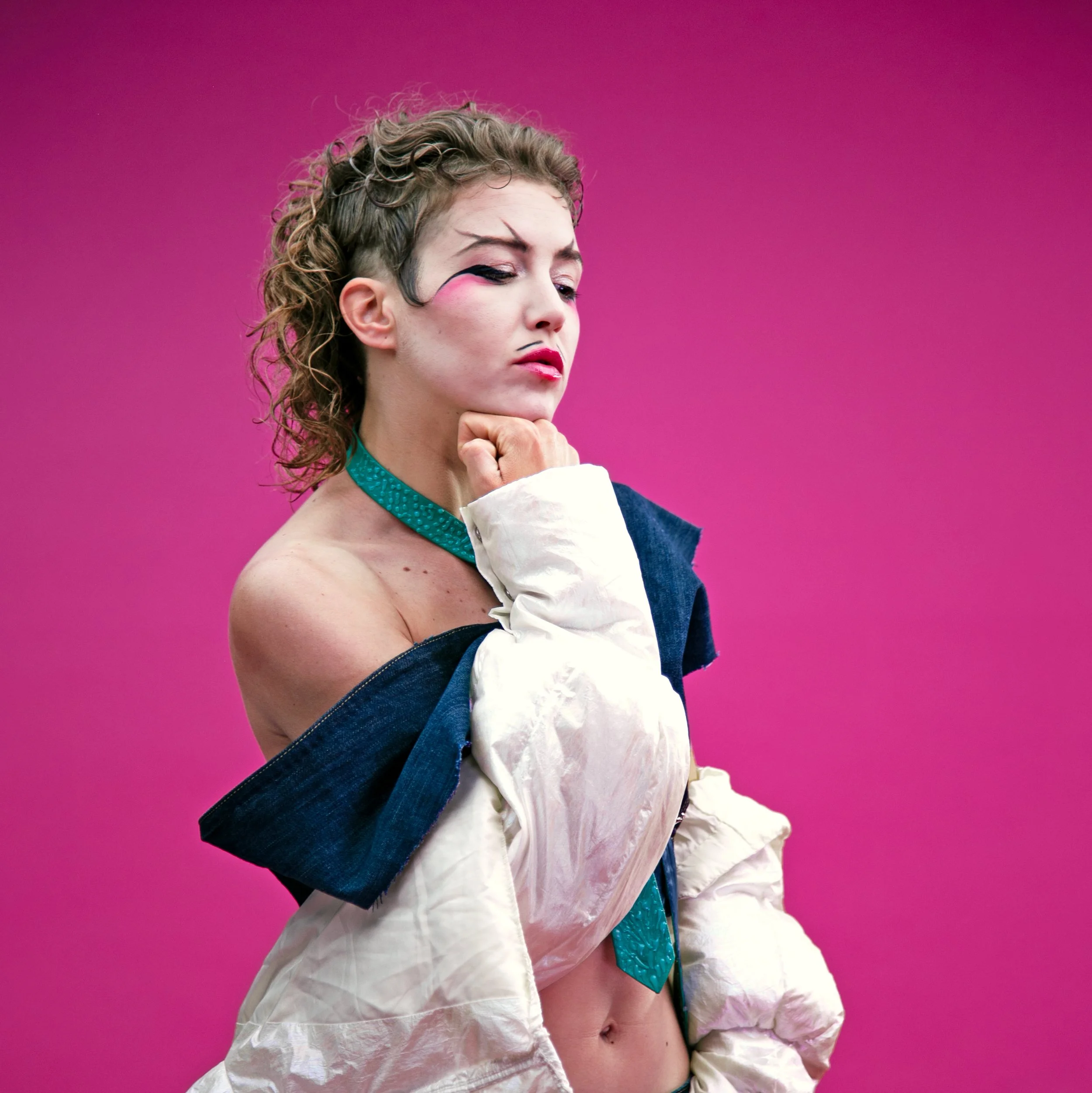 Bush.Ida blickt in nachdenklicher Pose zur Seite. Der Kopf ist auf die Faust gestützt. Das Makeup deutet einen Bart an.