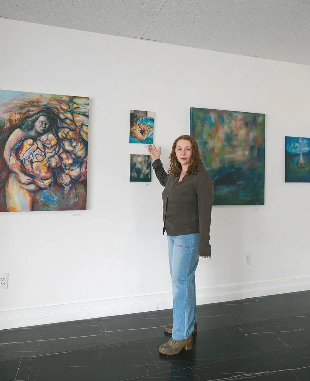 Woman standing in an art gallery pointing at paintings on a white wall.