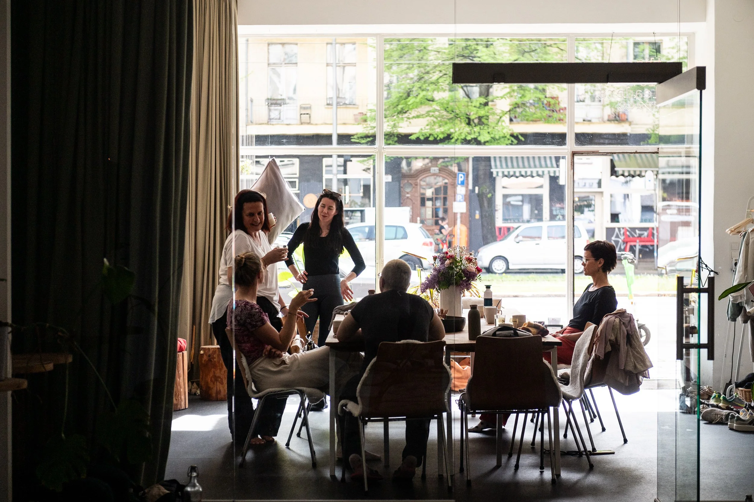 Menschen arbeiten an einem Tisch hinter einer Glastür. Man kann im Hintergrund eine Straße und Autos sehen.