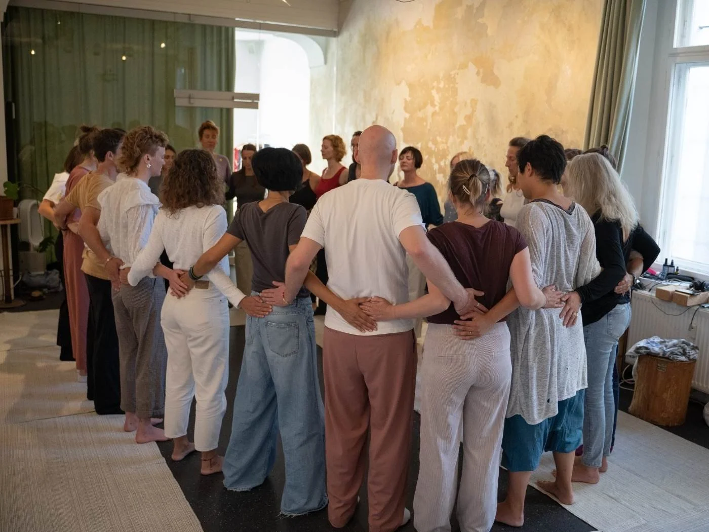 Ein geschlossener Raum mit Menschen die im Kreis stehen und sich sich an den Händen halten.
