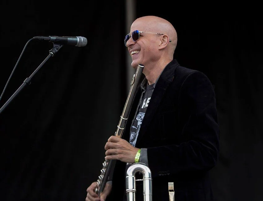 NYC flutist John Ragusa wearing sunglasses and holding his flute on stage.