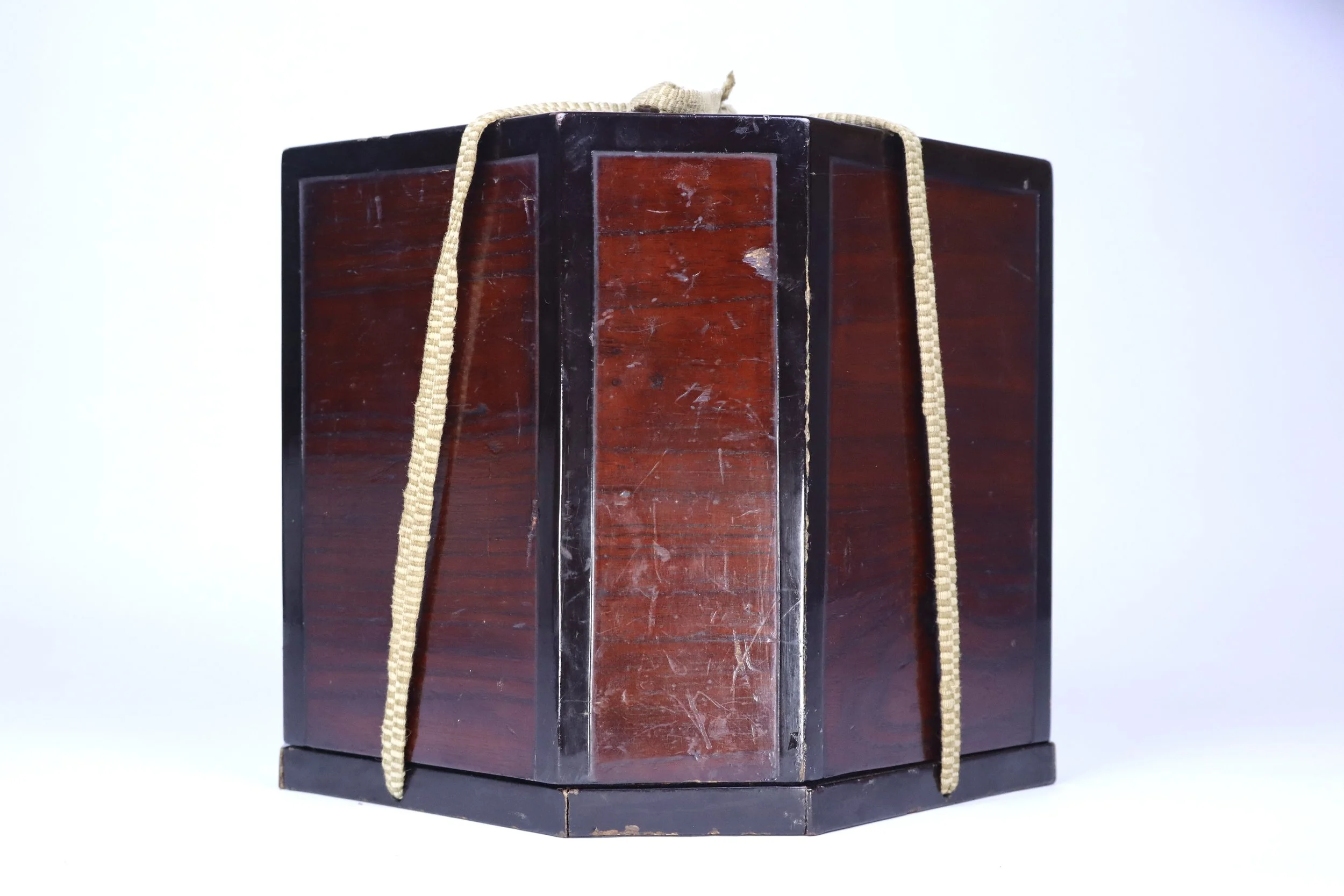 An antique wooden cube with a dark finish, bound by beige straps.