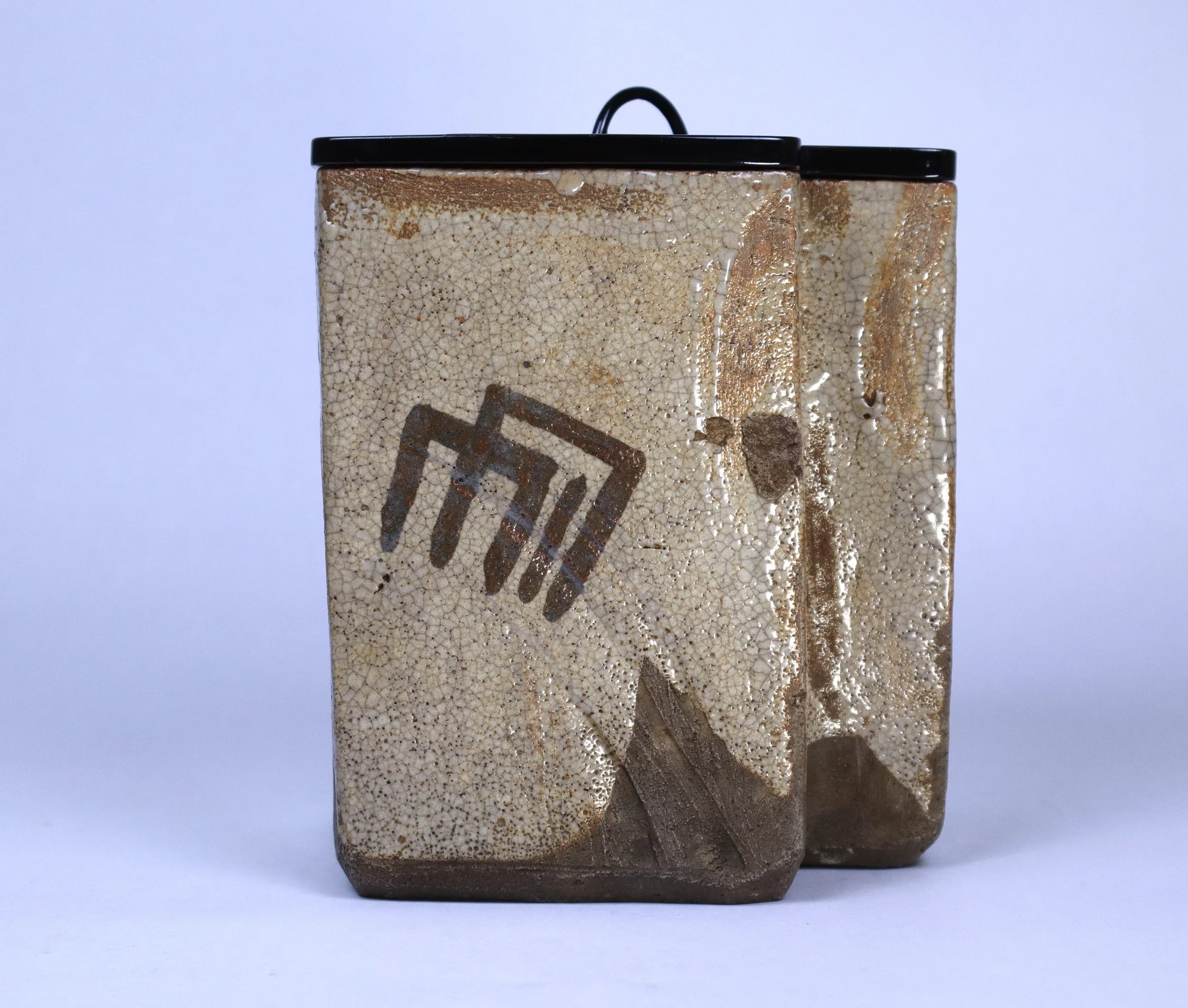 Two ceramic containers with black lids, one larger in front and one smaller behind, both featuring a beige and brown crackled glaze with a geometric black design.