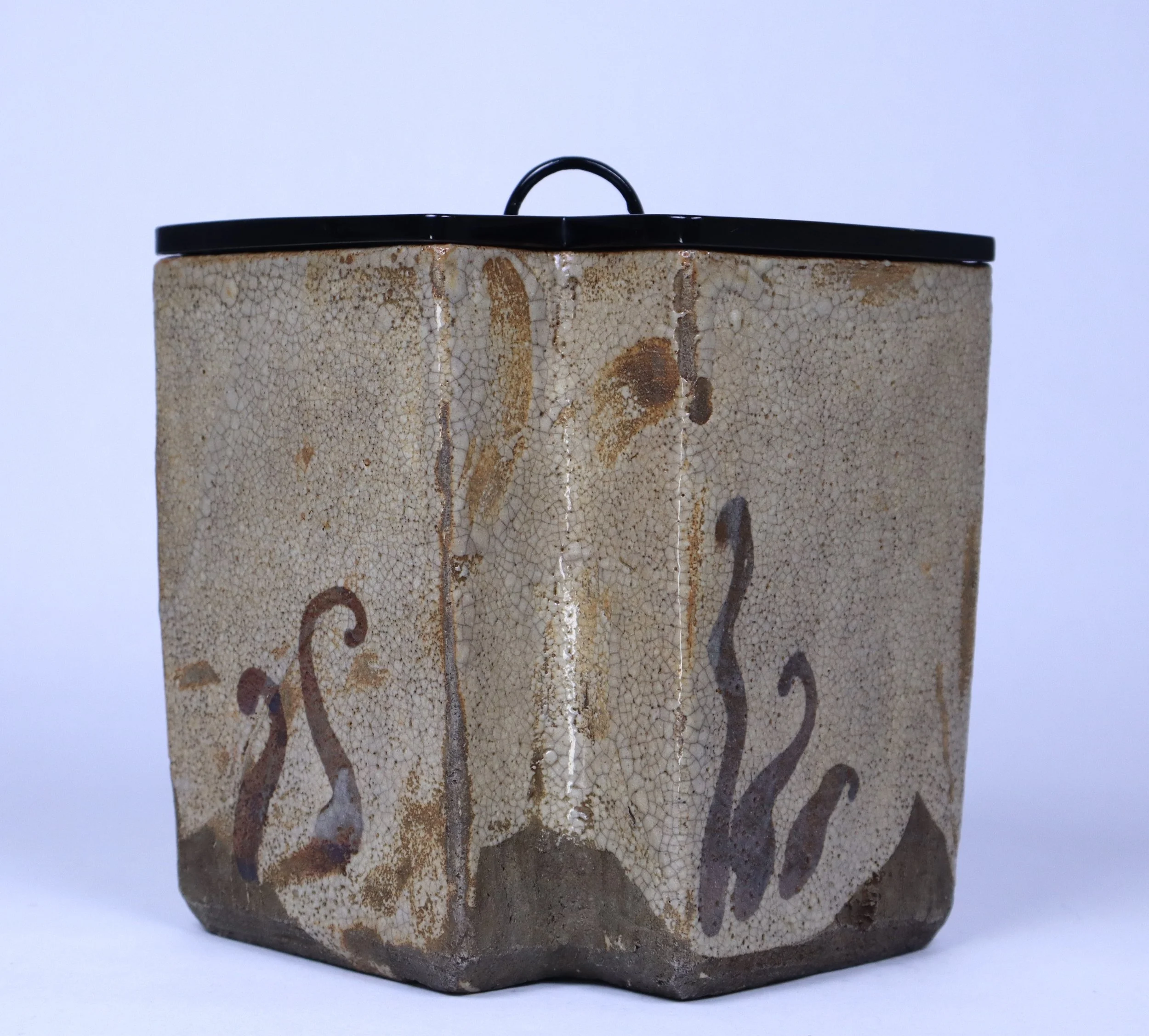 A rectangular ceramic container with a black lid, decorated with abstract flame-like designs in brown and purple on a crackled beige background.